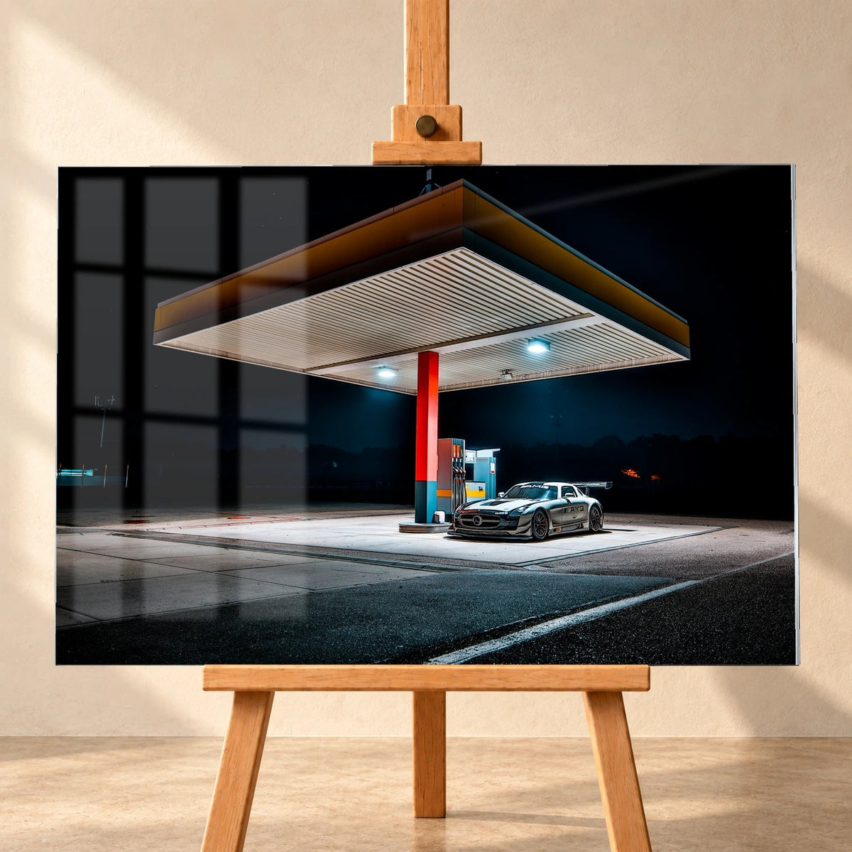 Als Acrylglas-Wandbild visualisierter Mercedes SLS GT3 an einer beleuchteten Tankstelle bei Nacht. Das querformatige Bild steht frontal auf einer Holzstaffelei; auf der Bildfläche sind Fensterreflexionen der inszenierten Umgebung sichtbar.