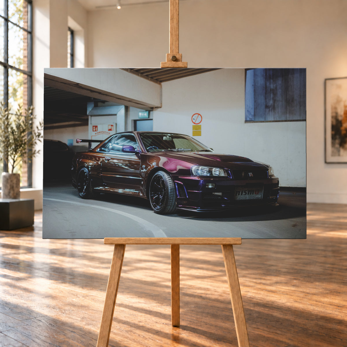 Dunkelvioletter Nissan Skyline R34 in einem Parkhaus, schräg von vorn fotografiert, mit schwarzen Rädern, großem Heckflügel und pink-violetten Lichtreflexionen auf der Karosserie; Visualisierung als Leinwand-Wandbild, auf einer Holzstaffelei in einem hellen Galerieraum.