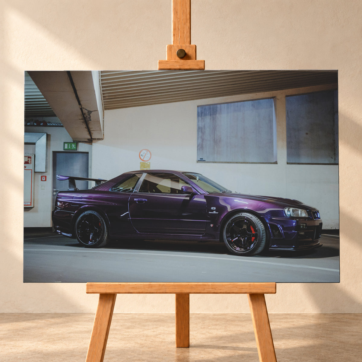 Violetter Nissan Skyline R34, nahezu seitlich mit der Front nach rechts, in einem hellen Parkgaragen-Innenraum; sichtbar sind schwarze Räder, rote Bremssättel und ein großer Heckflügel; Visualisierung als Leinwand-Wandbild, frontal auf einer Holzstaffelei.