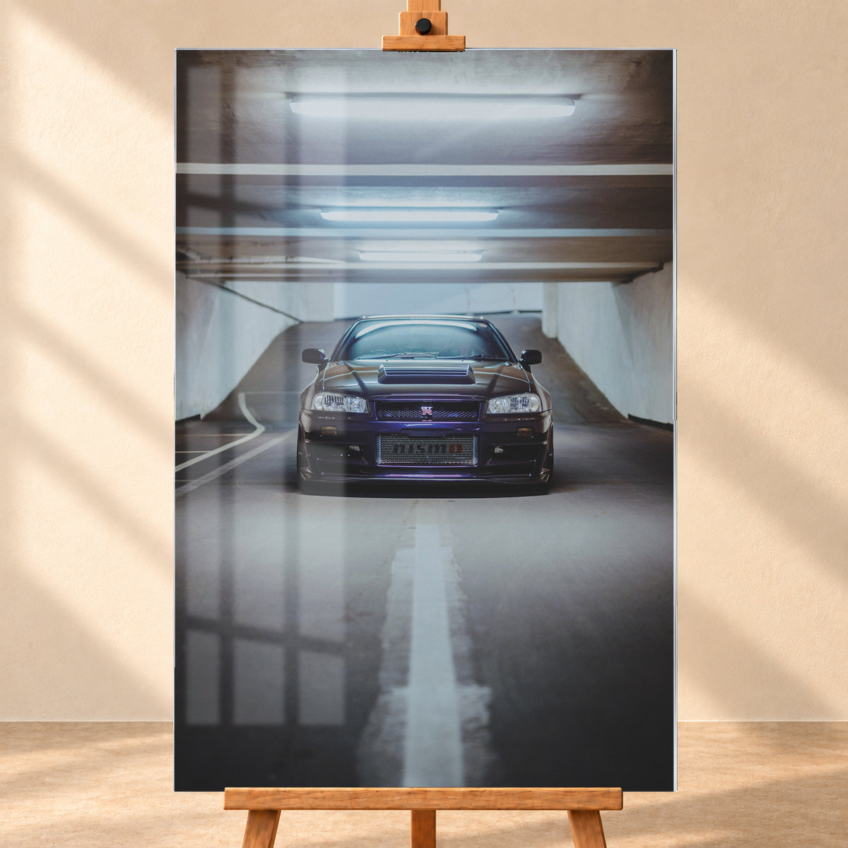 Dunkelvioletter Nissan Skyline R34 in zentraler Frontansicht auf der Zufahrt einer Parkgarage, beleuchtet von mehreren weißen Deckenleuchten und umgeben von grauen Wänden und Fahrbahnmarkierungen; Visualisierung als Acrylglas-Wandbild, frontal auf einer Holzstaffelei.
