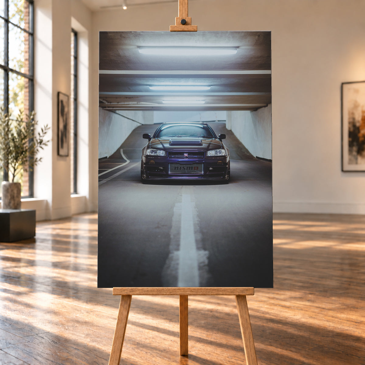 Dunkelvioletter Nissan Skyline R34 in zentraler Frontansicht auf der Zufahrt einer Parkgarage, beleuchtet von mehreren weißen Deckenleuchten und umgeben von grauen Wänden und Fahrbahnmarkierungen; Visualisierung als Leinwand-Wandbild, auf einer Holzstaffelei in einem hellen Galerieraum.