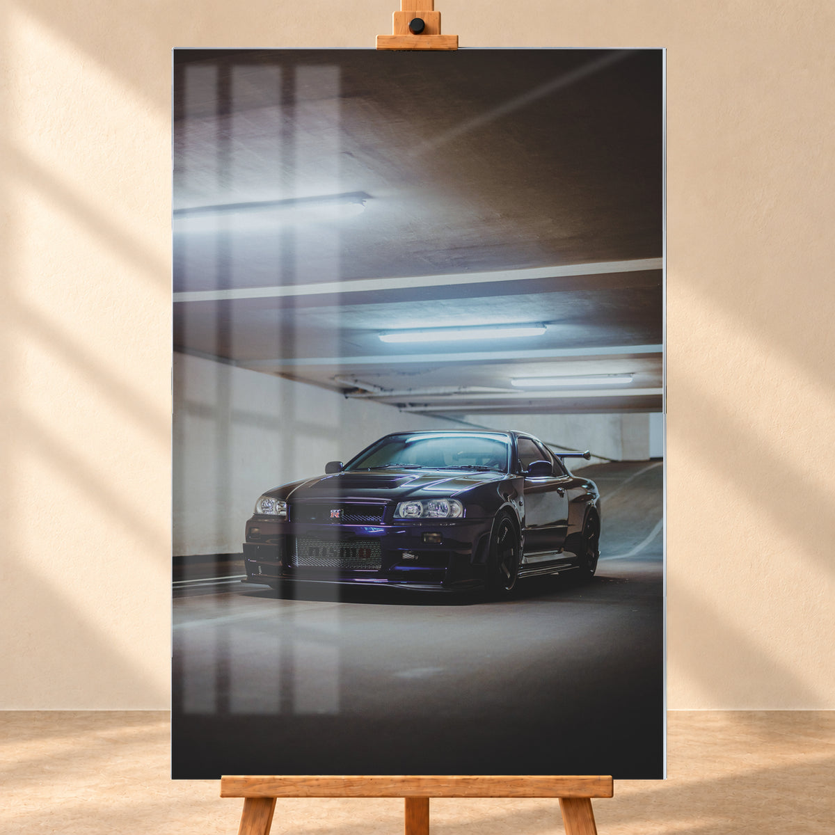 Dunkelvioletter Nissan Skyline R34 in Front-Dreiviertelansicht in einer Betonparkgarage. Kühle Deckenleuchten spiegeln sich auf der Karosserie; dunkle Räder, Seitenschweller und ein großer Heckflügel sind sichtbar. Das Hochformat zeigt viel dunkle Deckenfläche und eine ansteigende Rampe im Hintergrund; Visualisierung als Acrylglas-Wandbild, frontal auf einer Holzstaffelei.