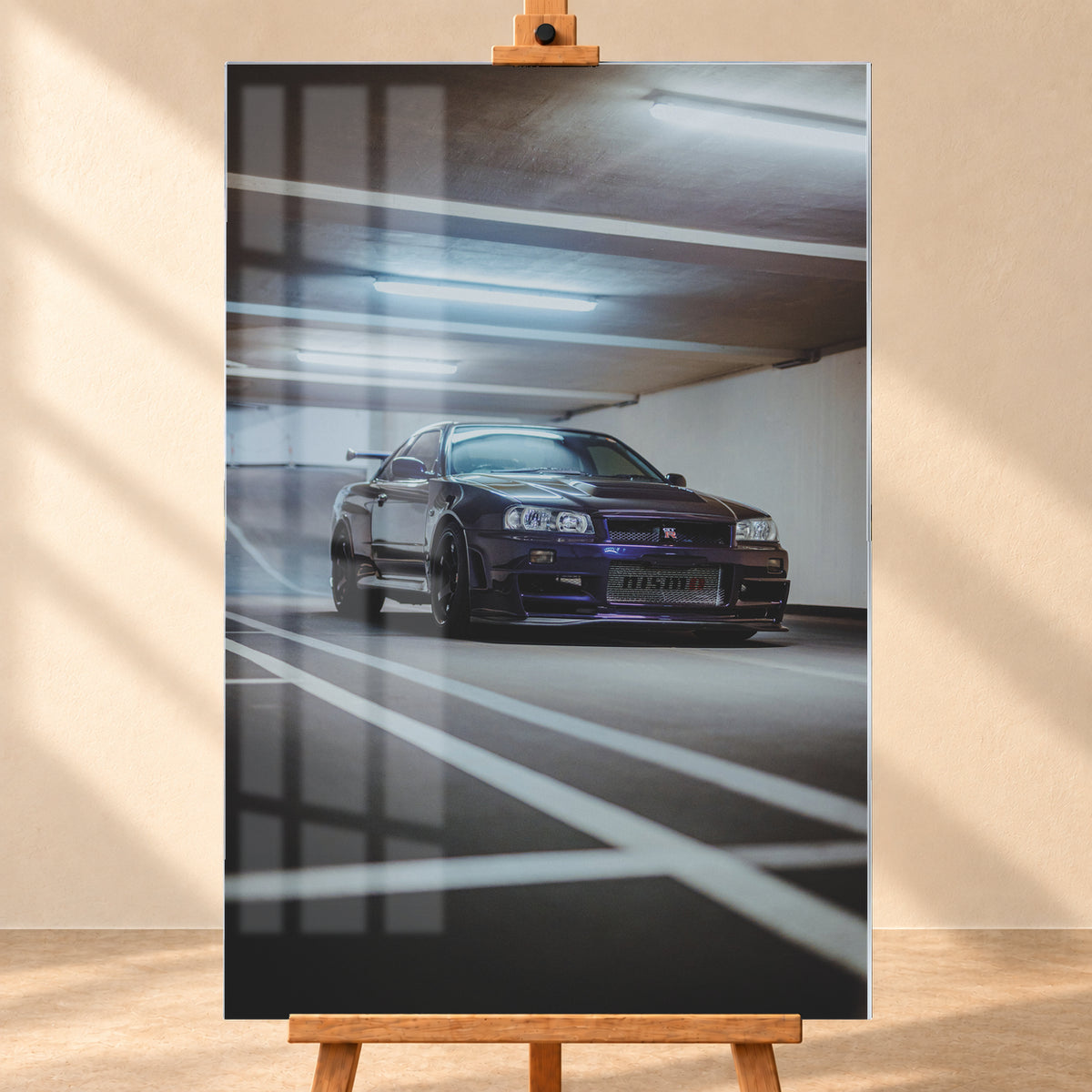 Dunkelvioletter Nissan Skyline R34 in niedriger Frontdreiviertelansicht in einer Beton-Parkgarage. Weiße Fahrbahnmarkierungen führen zum Fahrzeug; kühle Deckenleuchten spiegeln sich auf Haube und Scheibe. Sichtbar sind dunkle Räder und ein großer Heckflügel; Visualisierung als Acrylglas-Wandbild, frontal auf einer Holzstaffelei.