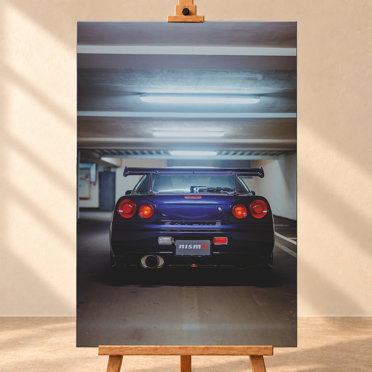Mittige Heckansicht eines dunkelvioletten Nissan Skyline R34 in einer Parkgarage. Vier runde rote Rückleuchten, davon die beiden inneren orange leuchtend, ein großer Heckflügel, ein rundes Auspuffendrohr und ein Nismo-Schriftzug sind unter kühlen, horizontalen Deckenleuchten zu sehen; Visualisierung als Leinwand-Wandbild, frontal auf einer Holzstaffelei.