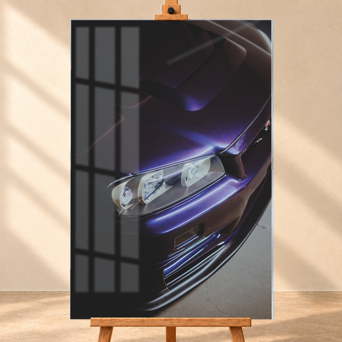 Steile Nahaufnahme der Front eines Nissan Skyline R34 in dunkelviolettem Lack mit Motorhaube, einem Scheinwerfer und Frontschürze; helle Reflexe zeichnen die Karosseriekanten vor einer überwiegend dunklen Umgebung nach; Visualisierung als Acrylglas-Wandbild, frontal auf einer Holzstaffelei.