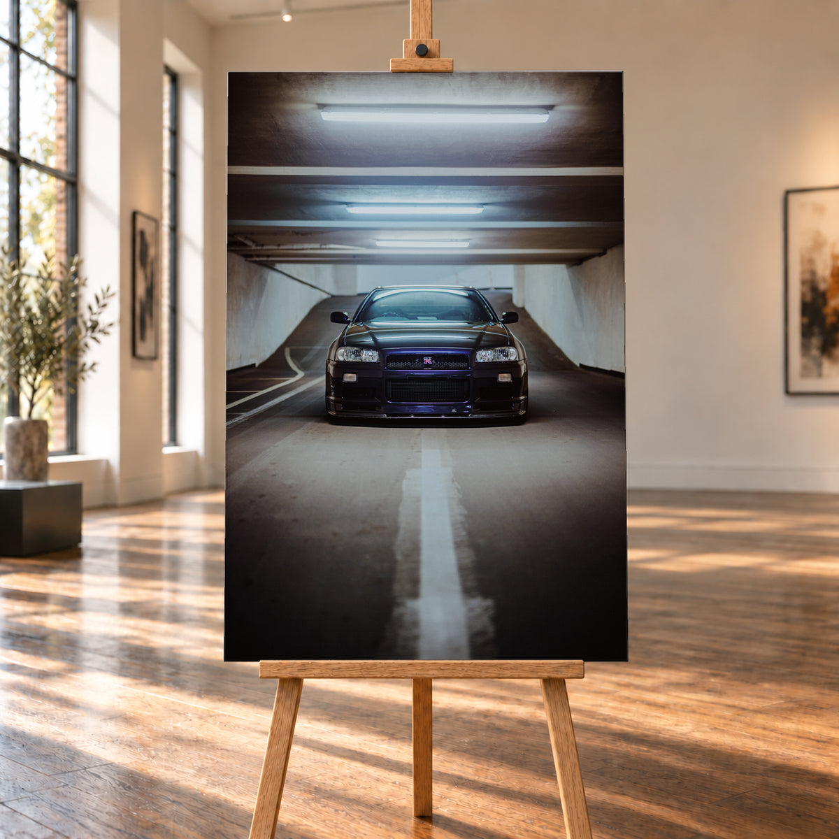 Dunkler Nissan Skyline R34 in frontaler Ansicht auf einer Betonrampe, unter kühlen weißen Deckenleuchten, mit mittiger Fahrbahnmarkierung und violettblauen Reflexen an Kühlergrill und Frontschürze; Visualisierung als Leinwand-Wandbild, auf einer Holzstaffelei in einem hellen Galerieraum.