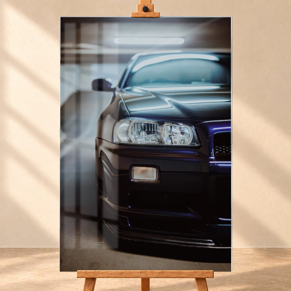 Dunkler Nissan Skyline in naher, leicht versetzter Frontansicht in einem Parkhaus. Sichtbar sind Scheinwerfer, Stoßfänger, Motorhaube, Windschutzscheibe und Seitenspiegel mit kühlen blau-violetten Lichtreflexen; Visualisierung als Acrylglas-Wandbild, frontal auf einer Holzstaffelei.