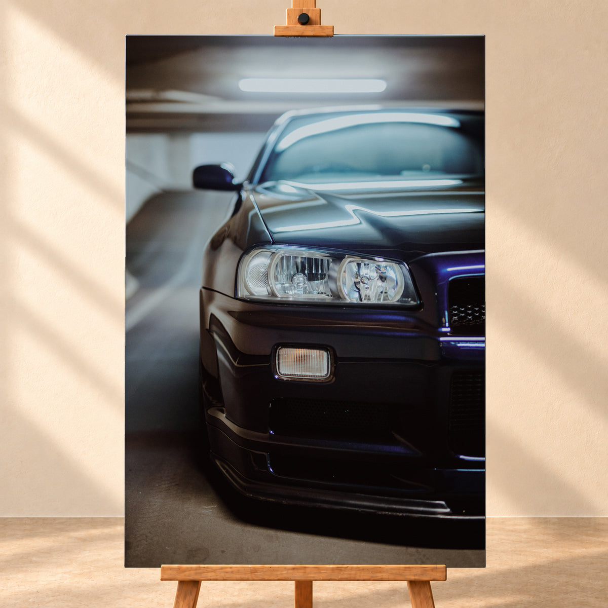 Dunkler Nissan Skyline in naher, leicht versetzter Frontansicht in einem Parkhaus. Sichtbar sind Scheinwerfer, Stoßfänger, Motorhaube, Windschutzscheibe und Seitenspiegel mit kühlen blau-violetten Lichtreflexen; Visualisierung als Leinwand-Wandbild, frontal auf einer Holzstaffelei.