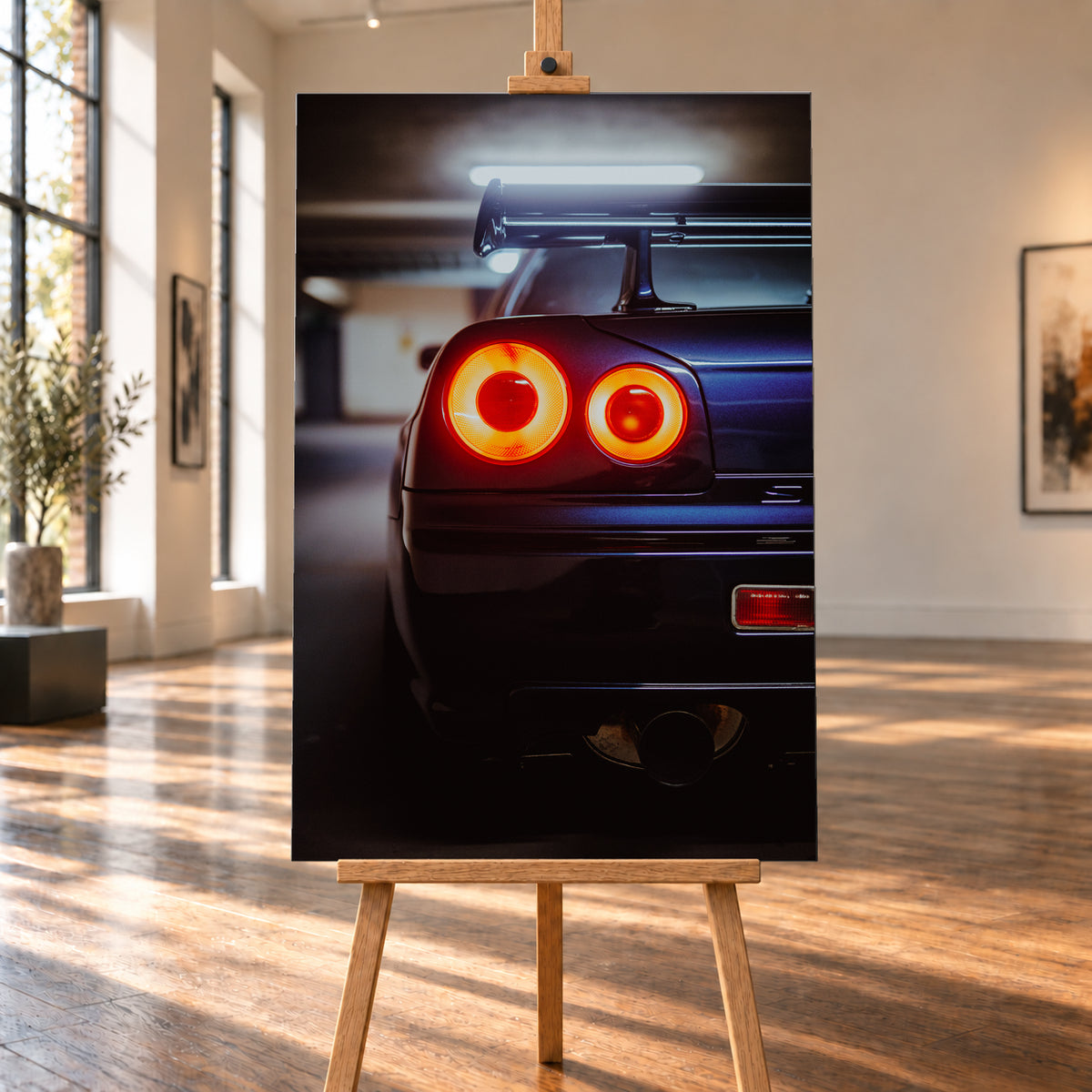 Nahaufnahme der Heckpartie eines dunklen Nissan Skyline R34 V-Spec mit zwei sichtbaren, rot-orange leuchtenden Rundrückleuchten, großem Heckflügel und rundem Auspuffendrohr vor unscharfem, kühl beleuchtetem Hintergrund; Visualisierung als Leinwand-Wandbild, auf einer Holzstaffelei in einem hellen Galerieraum.