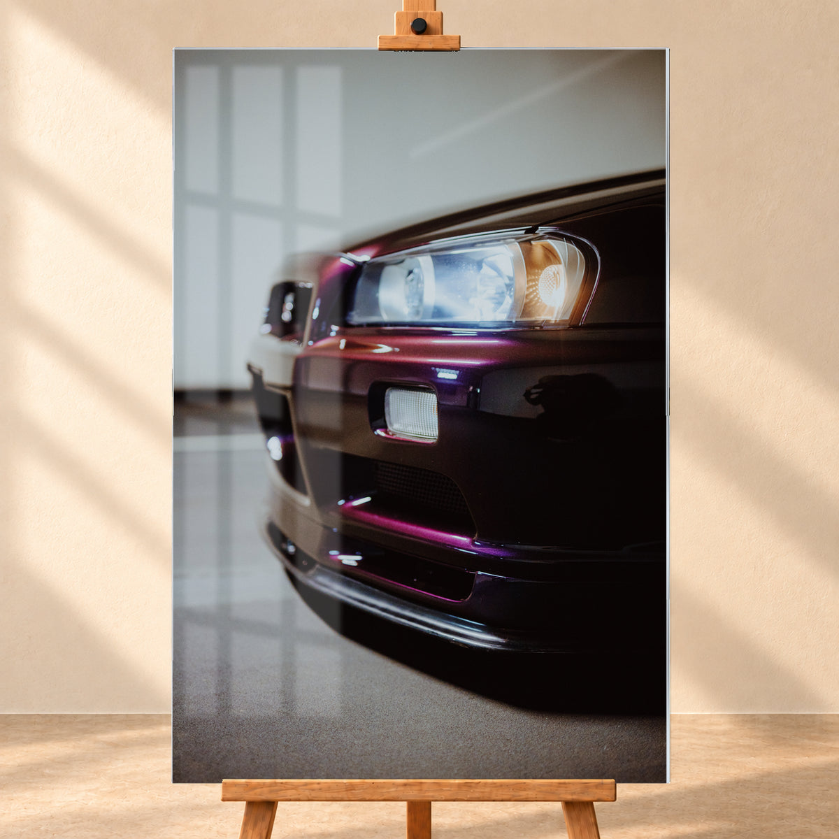 Nahaufnahme der Front eines dunklen, bordeauxviolett wirkenden Nissan Skyline V-Spec aus niedriger, schräger Perspektive. Ein rechteckiger Scheinwerfer mit kühlen und warmen Lichtanteilen dominiert die rechte Bildhälfte. Darunter sind Frontschürze, Leuchte und Lufteinlass zu sehen; eine hellgraue Wand und ein grauer Boden bilden den unscharfen Hintergrund; Visualisierung als Acrylglas-Wandbild, frontal auf einer Holzstaffelei.