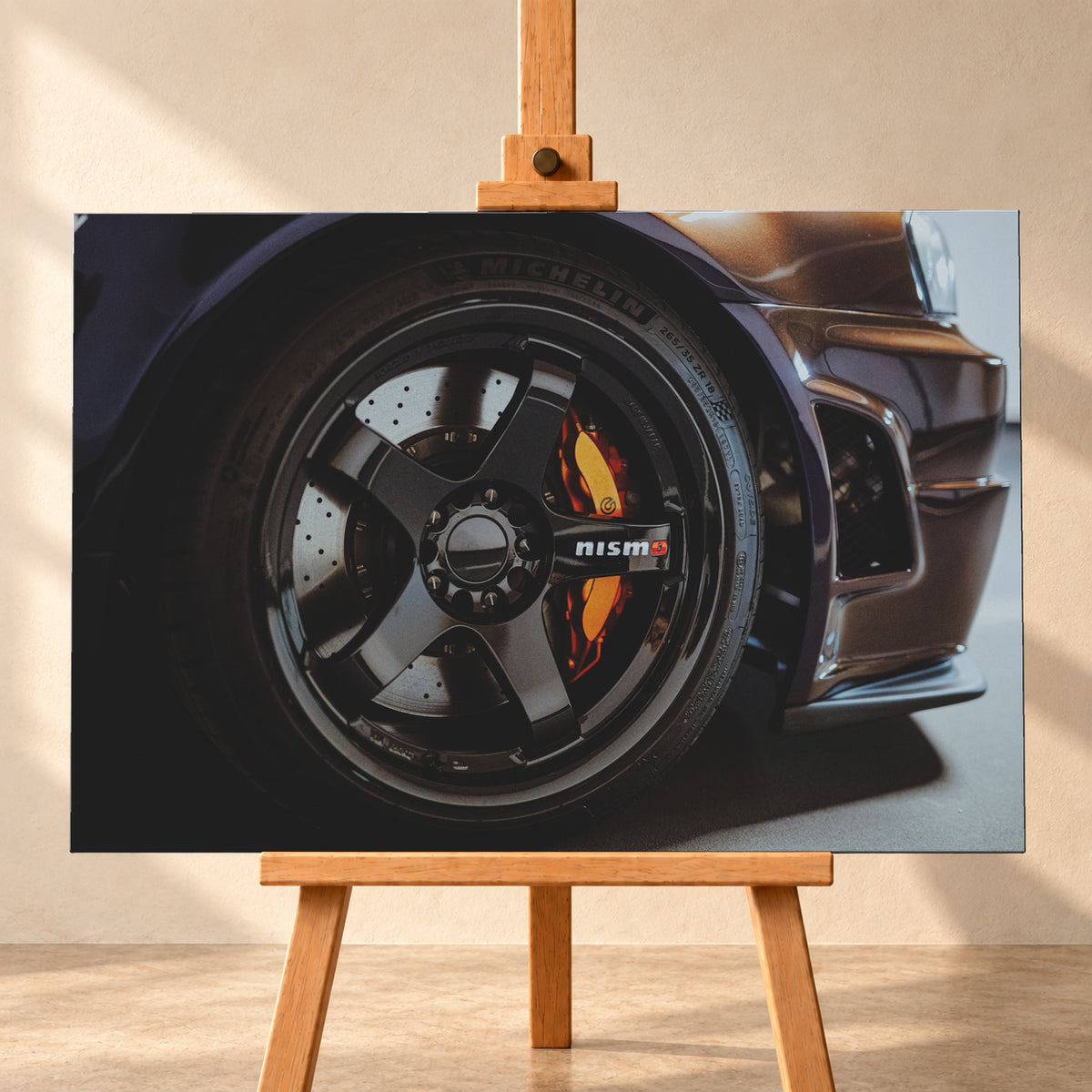 Nahaufnahme der Frontpartie eines dunkelviolett-bronze schimmernden Nissan Skyline R34 mit schwarzem Rad, sichtbarem NISMO-Schriftzug, gelochter Bremsscheibe und orange-rotem Bremssattel bei kontrastreichem Licht; Visualisierung als Leinwand-Wandbild, frontal auf einer Holzstaffelei.