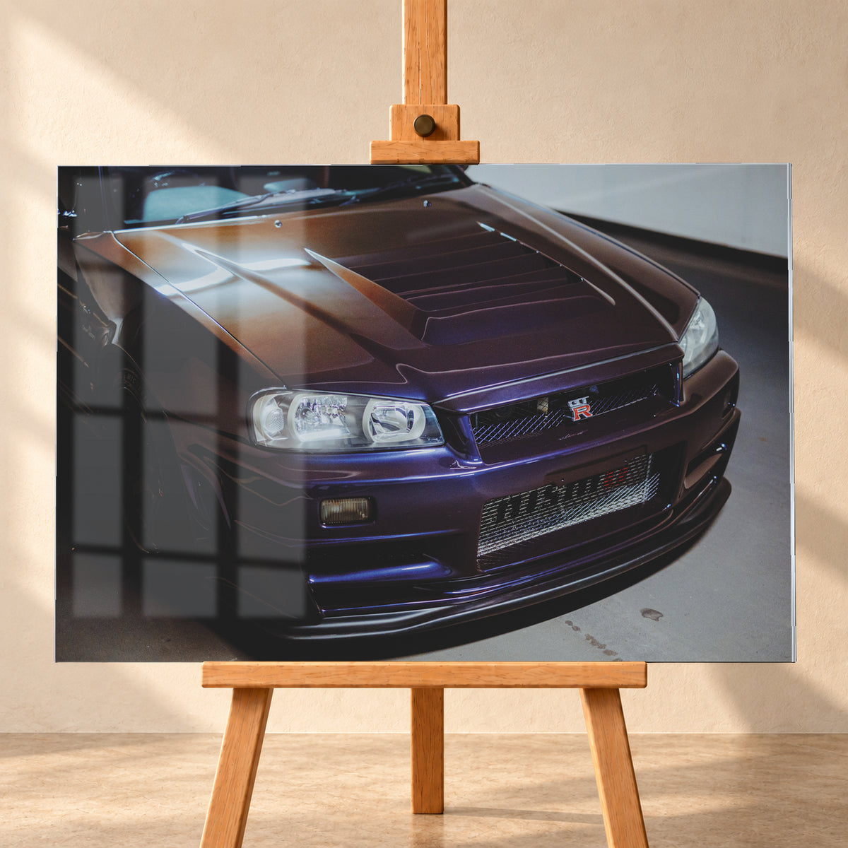 Nahes Frontporträt eines Nissan Skyline R34 in violett schimmerndem Lack, leicht von oben fotografiert, mit konturierter Motorhaube, Scheinwerfern, Kühlergrill und breiten Lufteinlässen in einem hellen Innenraum; Visualisierung als Acrylglas-Wandbild, frontal auf einer Holzstaffelei.