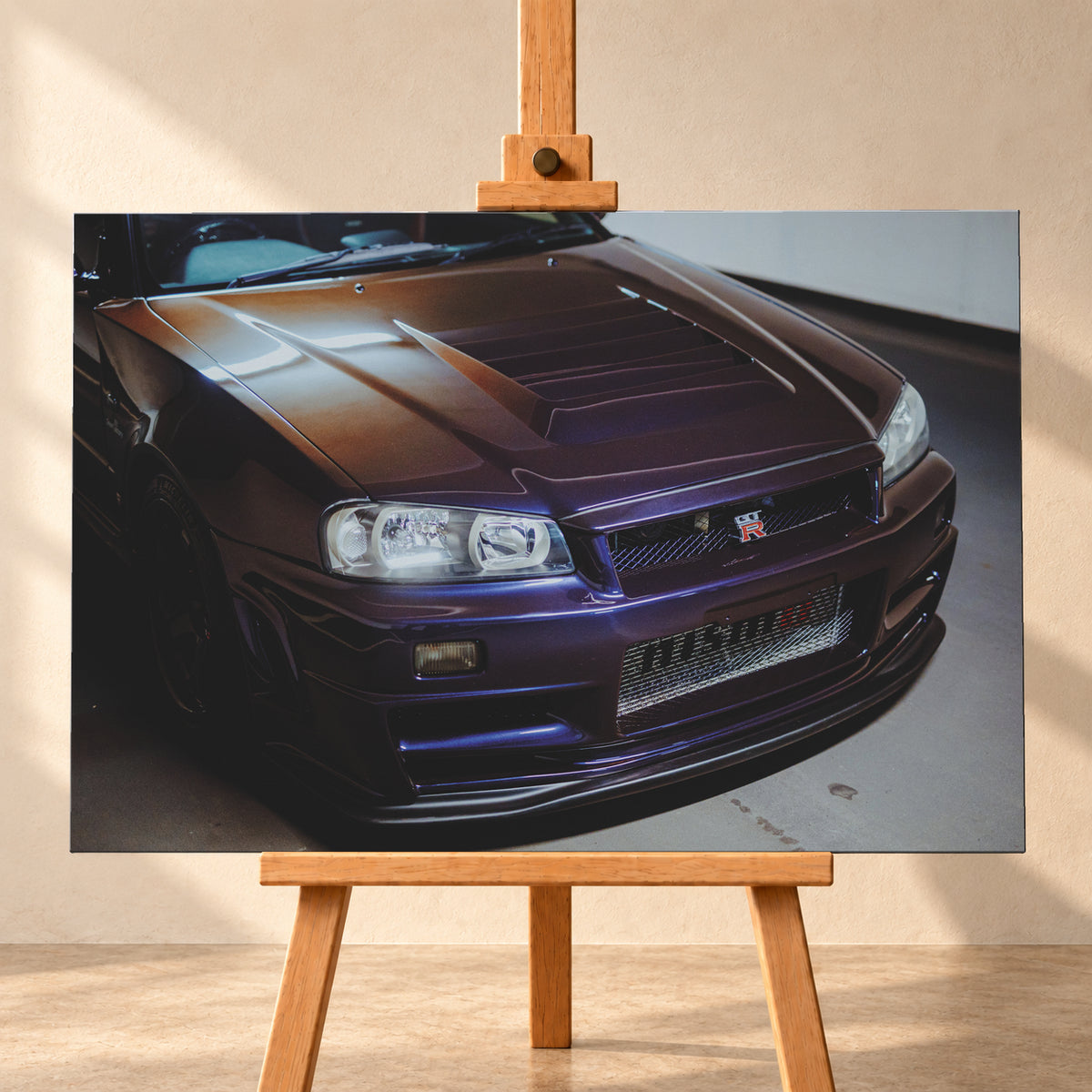 Nahes Frontporträt eines Nissan Skyline R34 in violett schimmerndem Lack, leicht von oben fotografiert, mit konturierter Motorhaube, Scheinwerfern, Kühlergrill und breiten Lufteinlässen in einem hellen Innenraum; Visualisierung als Leinwand-Wandbild, frontal auf einer Holzstaffelei.