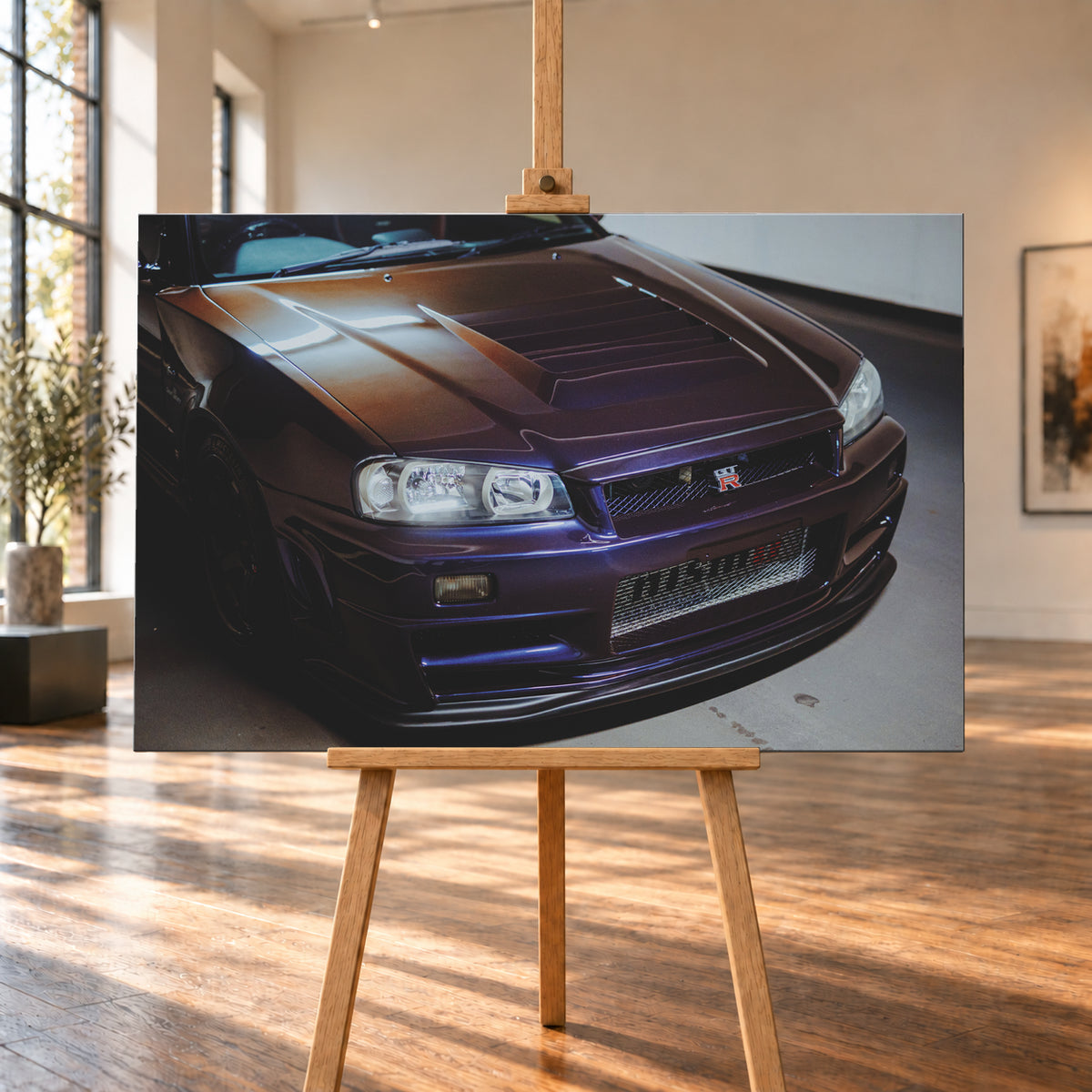 Nahes Frontporträt eines Nissan Skyline R34 in violett schimmerndem Lack, leicht von oben fotografiert, mit konturierter Motorhaube, Scheinwerfern, Kühlergrill und breiten Lufteinlässen in einem hellen Innenraum; Visualisierung als Leinwand-Wandbild, auf einer Holzstaffelei in einem hellen Galerieraum.