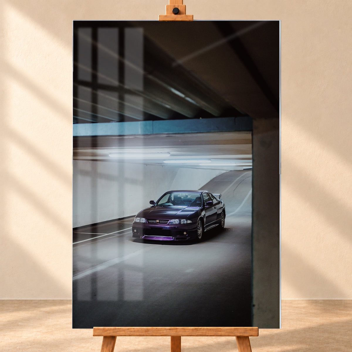 Dunkelvioletter Nissan Skyline in vorderer Dreiviertelansicht in einer Beton-Tiefgarage, beleuchtet von kühlen Deckenleuchten; Fahrbahnlinien und eine Rampe liegen im Hintergrund; Visualisierung als Acrylglas-Wandbild, frontal auf einer Holzstaffelei.