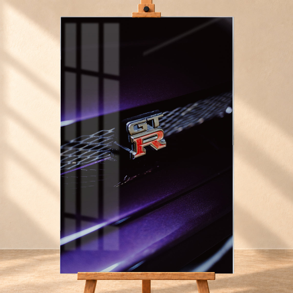 Nahaufnahme eines rot-silbernen GT-R-Emblems an einem dunklen Frontgrill, beleuchtet von violettem Licht und umgeben von tiefen Schatten; Visualisierung als Acrylglas-Wandbild, frontal auf einer Holzstaffelei.