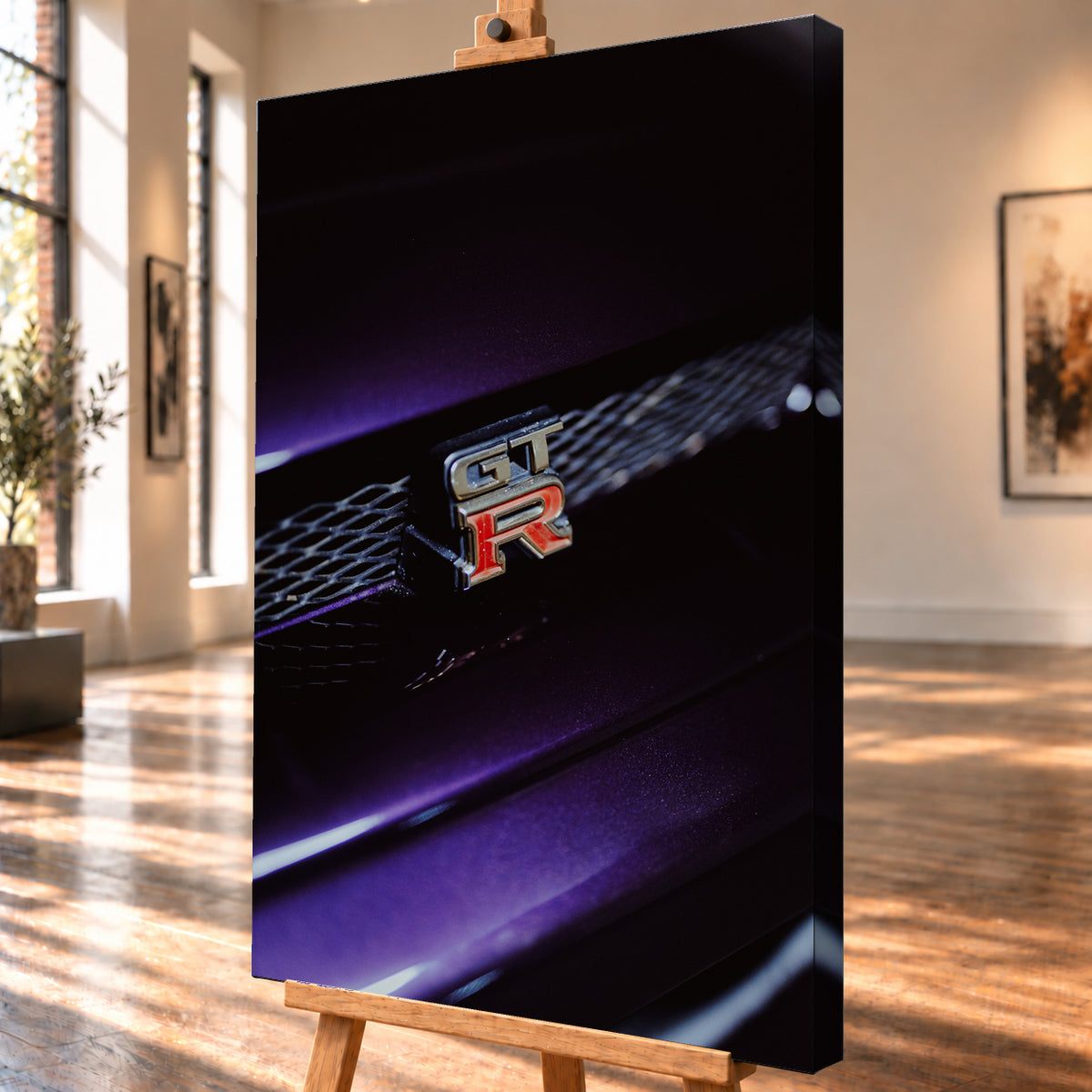 Nahaufnahme eines rot-silbernen GT-R-Emblems an einem dunklen Frontgrill, beleuchtet von violettem Licht und umgeben von tiefen Schatten; Visualisierung als Leinwand-Wandbild, schräg von der Seite auf einer Holzstaffelei.
