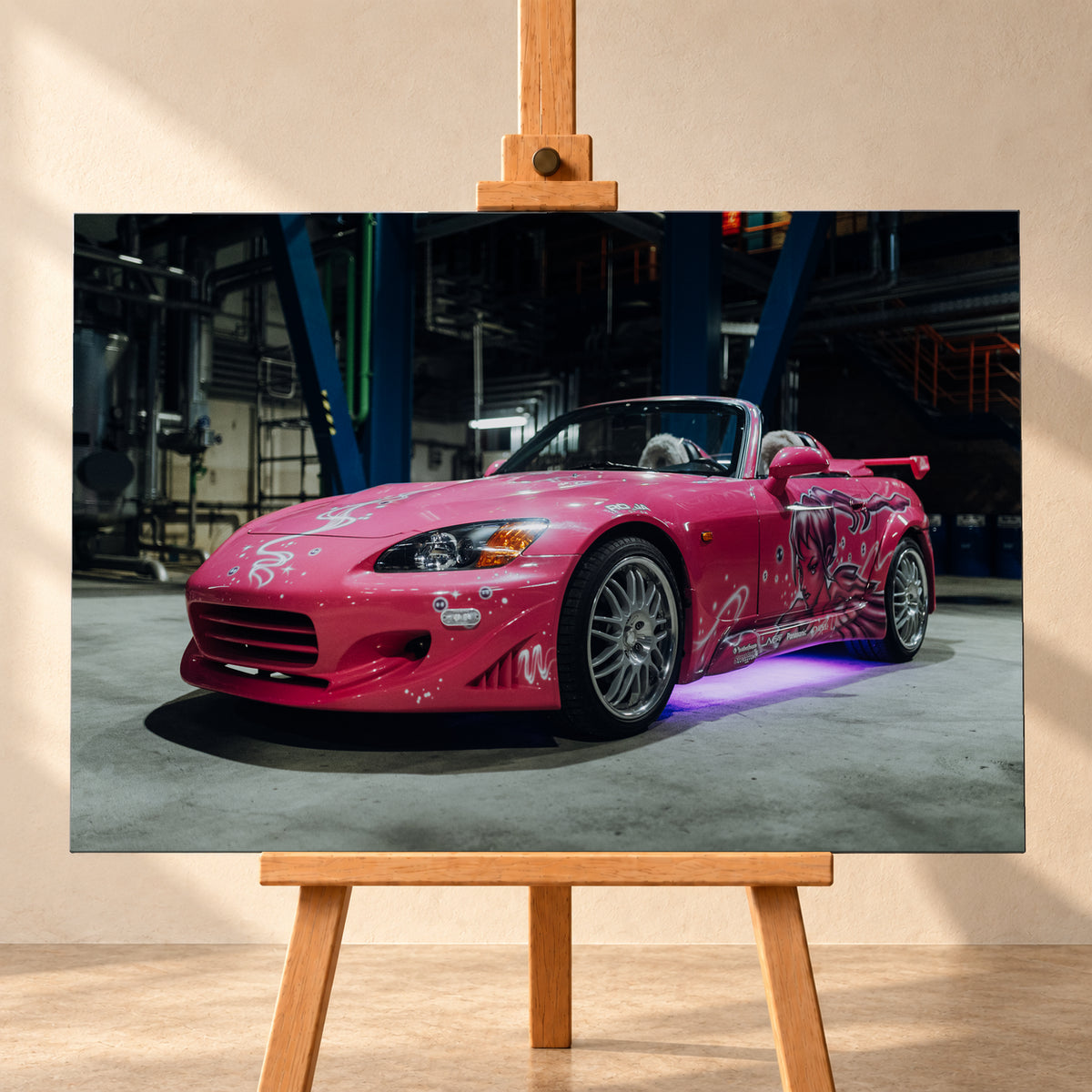 Pinker Honda S2000 als offener Roadster in Front-Dreiviertelansicht auf einem Betonboden in einer dunklen Industriehalle; sichtbar sind weiße Dekorgrafiken, eine große Frauenfigur an der Seite, silberne Mehrspeichenräder, ein Heckflügel und violett-blaues Licht unter dem Fahrzeug; Visualisierung als Leinwand-Wandbild, frontal auf einer Holzstaffelei.