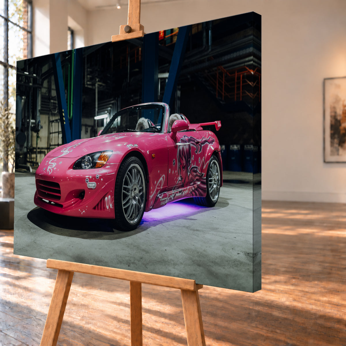 Pinker Honda S2000 als offener Roadster in Front-Dreiviertelansicht auf einem Betonboden in einer dunklen Industriehalle; sichtbar sind weiße Dekorgrafiken, eine große Frauenfigur an der Seite, silberne Mehrspeichenräder, ein Heckflügel und violett-blaues Licht unter dem Fahrzeug; Visualisierung als Leinwand-Wandbild, schräg von der Seite auf einer Holzstaffelei.