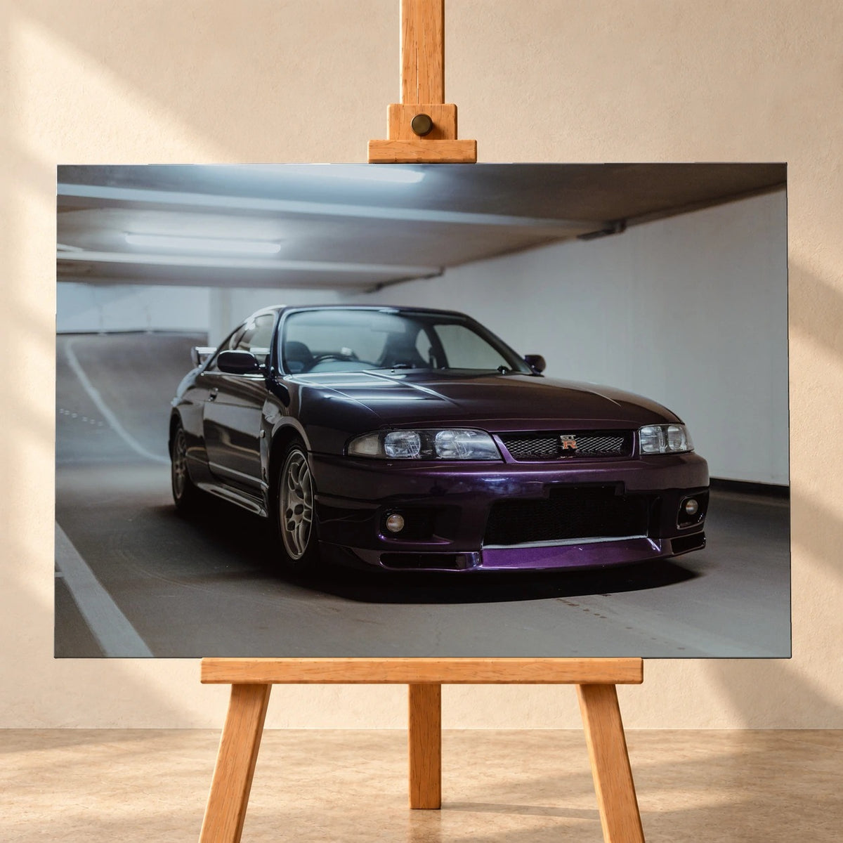 Frontale Visualisierung eines Leinwandbilds im Querformat auf einer Holzstaffelei vor heller Wand. Das Motiv zeigt einen dunkelvioletten Nissan Skyline GT-R R33 schräg von vorn in einer Tiefgarage.