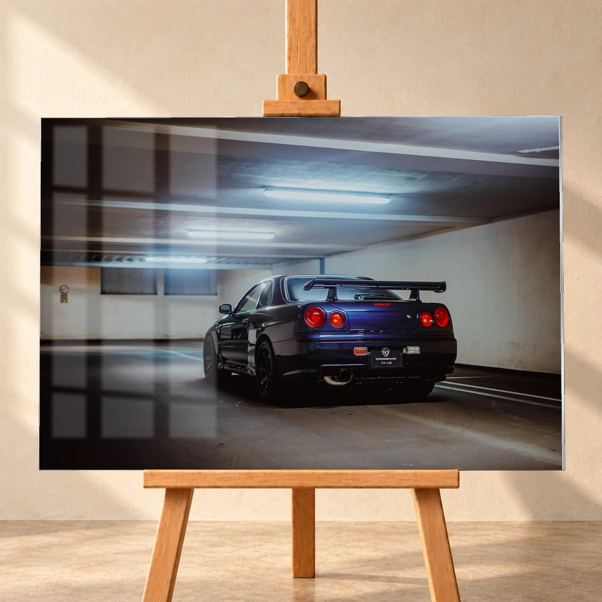 Frontale Visualisierung eines Acrylglas-Wandbilds auf einer Holzstaffelei vor heller Wand. Fensterspiegelungen überlagern die linke Bildfläche. Das Motiv zeigt einen dunkelvioletten Nissan Skyline R34 schräg von hinten in einer Tiefgarage, mit großem Heckflügel und runden roten Rückleuchten.