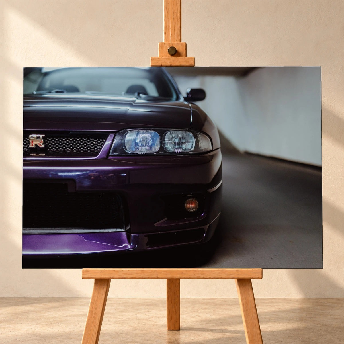 Visualisierung eines querformatigen Leinwandbilds auf einer Holzstaffelei vor einer hellen Wand. Das Motiv zeigt die violette Front eines Nissan Skyline GT-R R33 mit Scheinwerfern und GT-R-Emblem im Kühlergrill.
