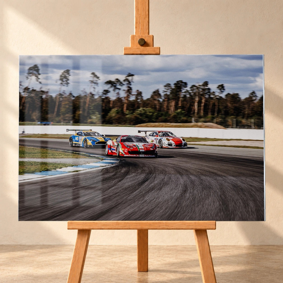 Aston Martin, Porsche und Ferrari GT3 fahren dicht gestaffelt durch eine Kurve; die Mehrwagen-Szene zeigt echtes Renngeschehen. Motiv „Racing Echo“ als Acrylglas-Wandbild, frontal auf einer Holzstaffelei.