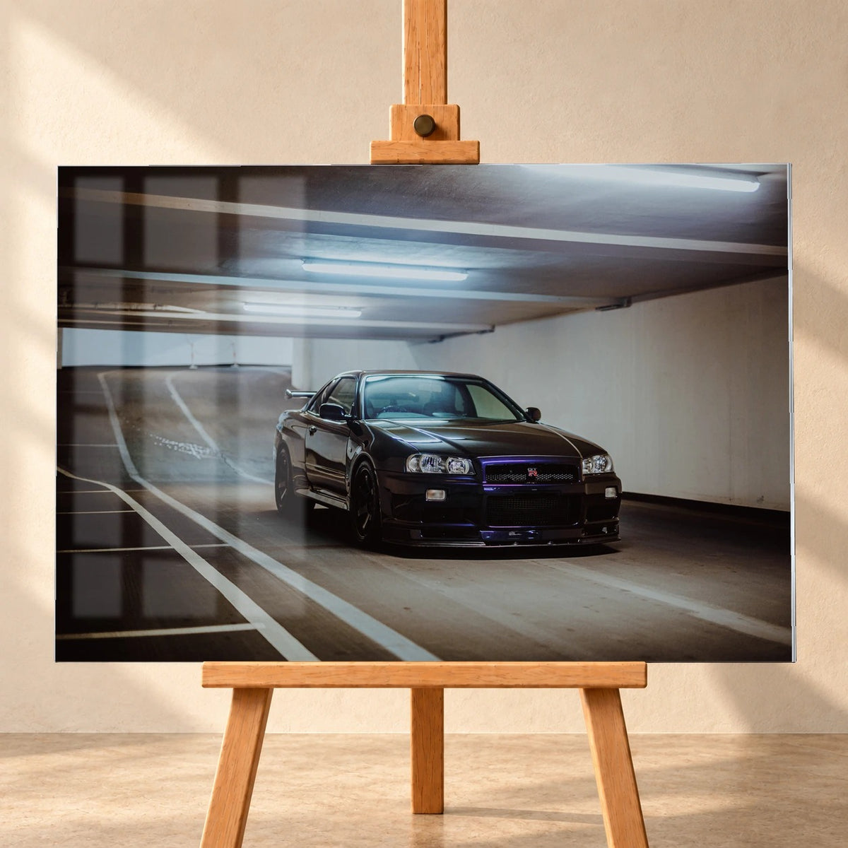 Frontal dargestelltes Acrylglas-Wandbild auf einer Holzstaffelei als Produktvisualisierung. Das Tiefgaragenmotiv mit einem dunkelvioletten Nissan Skyline GT-R R34 wird links von sichtbaren Fensterreflexionen überlagert.