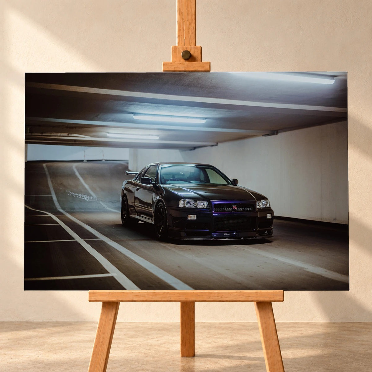 Visualisierung eines querformatigen Leinwandbilds auf einer Holzstaffelei vor einer hellen Wand. Das Motiv zeigt einen dunkelvioletten Nissan Skyline GT-R R34 in vorderer Dreiviertelansicht in einer Tiefgarage.