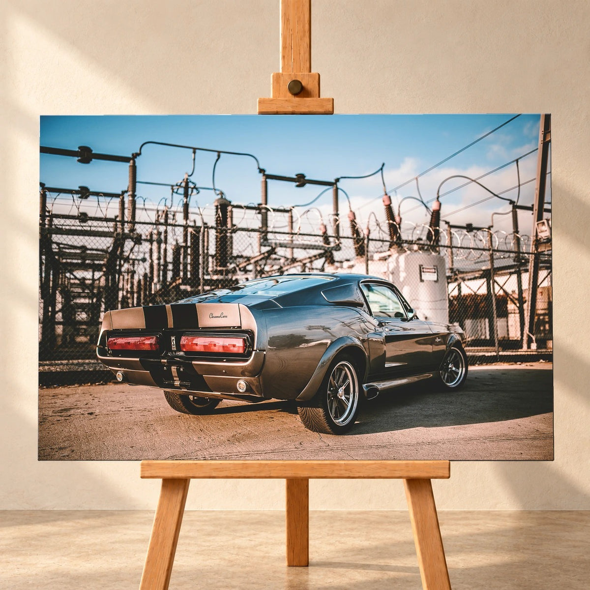 Visualisierung einer querformatigen Leinwand auf einer Holzstaffelei vor heller Wand. Das Motiv zeigt den grauen Ford Mustang Shelby GT500 „Eleanor“ mit schwarzen Streifen schräg von hinten vor einem umzäunten Umspannwerk.