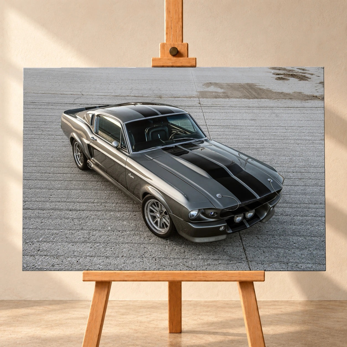 Visualisierung eines querformatigen Leinwandbilds, frontal auf einer Holzstaffelei vor heller Wand. Das Motiv zeigt Eleanor, einen grauen Ford Mustang Shelby GT500 mit schwarzen Doppelstreifen, schräg von vorn und oben auf einer Betonfläche.