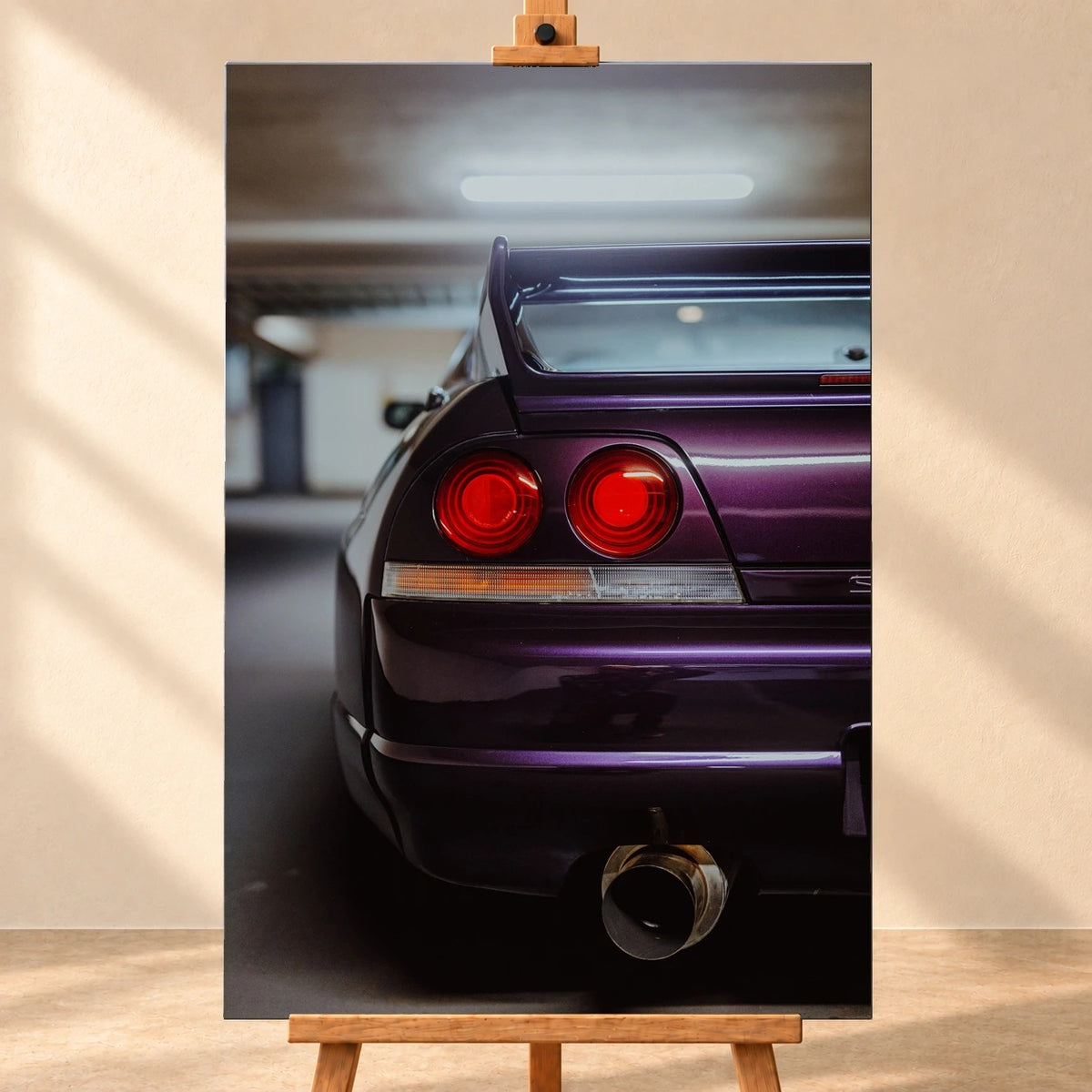Visualisierung eines hochformatigen Leinwandbildes auf einer Holzstaffelei vor beiger Wand, frontal gezeigt. Das Motiv zeigt die violette Heckpartie eines Nissan Skyline R33 mit zwei runden roten Rückleuchten, Heckflügel und großem Auspuffendrohr.