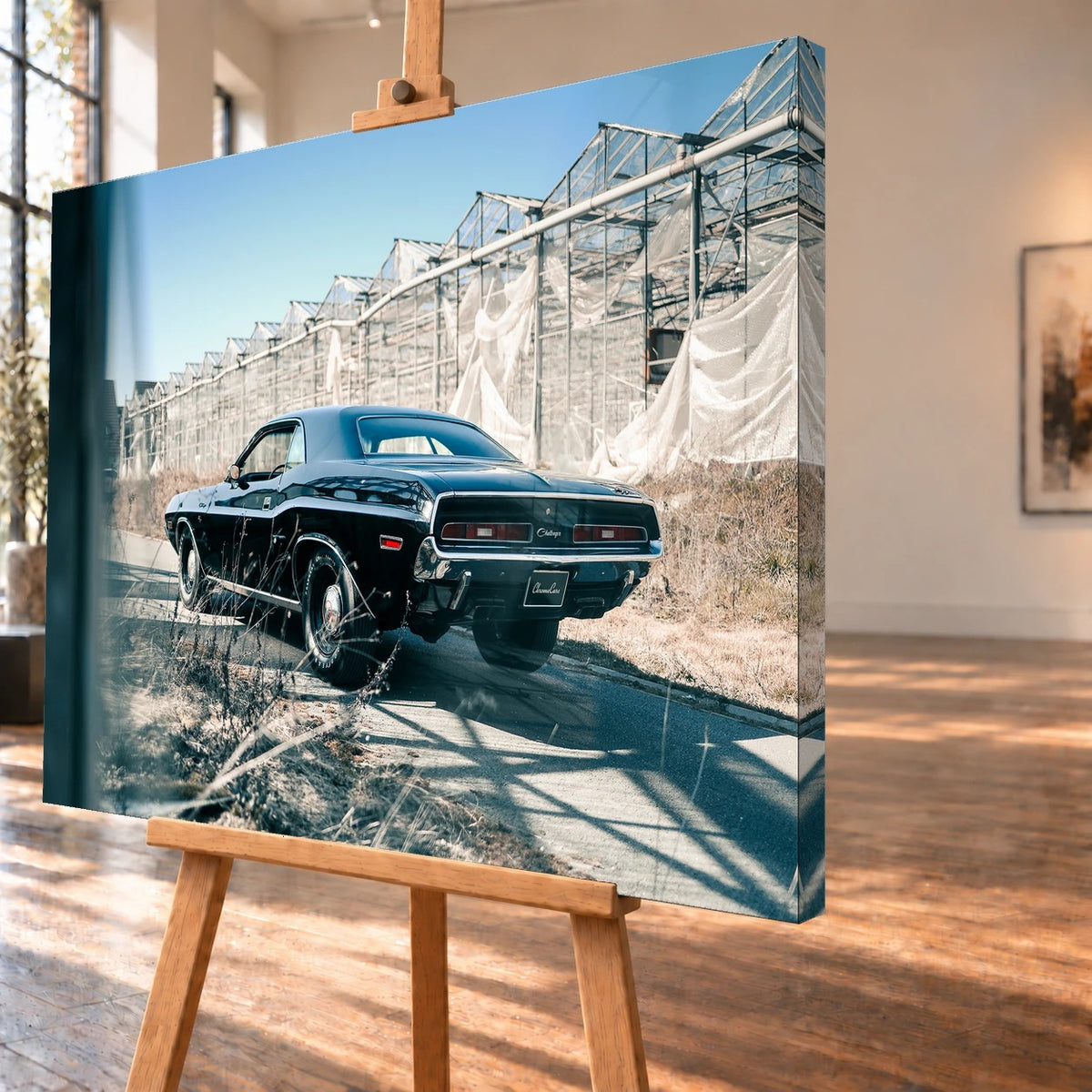 Schrägansicht eines Leinwandbilds als Visualisierung auf einer Staffelei; das Motiv setzt sich über die sichtbare rechte Seitenkante fort. Ein schwarzer Dodge Challenger 426 Hemi (1971) steht mit dem Heck zum Betrachter auf einem Weg neben Gewächshäusern.