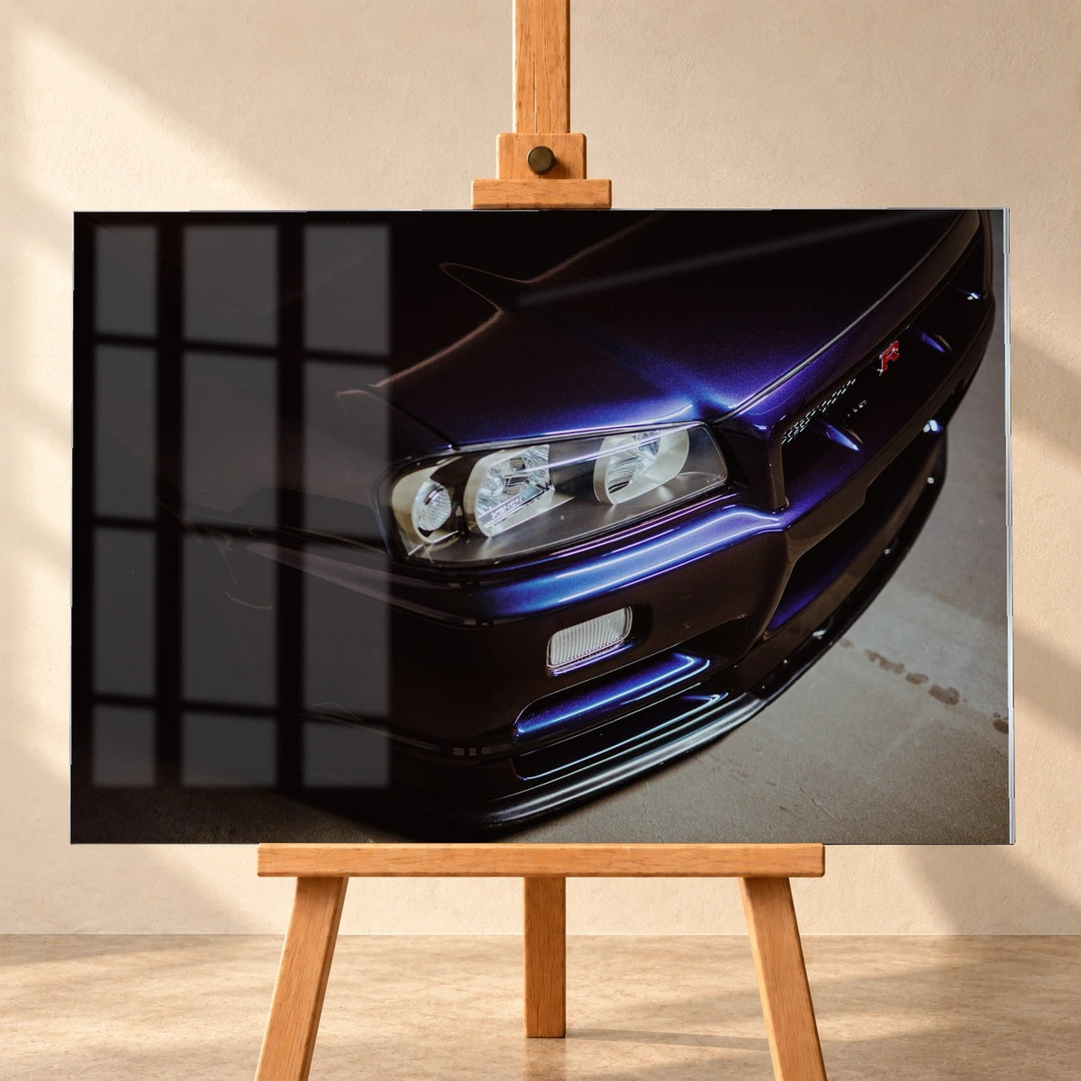Visualisierung eines Acrylglasbilds im Querformat auf einer Holzstaffelei vor heller Wand. Über dem Motiv der dunkelvioletten Front eines Nissan Skyline GT-R R34 mit Scheinwerfer und blauvioletten Lackreflexen liegt links die Spiegelung eines Sprossenfensters.