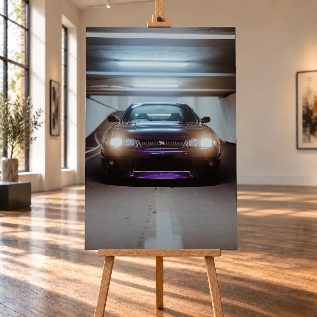 Raumvisualisierung mit einem hochformatigen Leinwandbild auf einer Holzstaffelei in einem hellen Raum mit großen Fenstern und Holzboden. Das Bild zeigt einen violetten Nissan Skyline GT-R R33 von vorn mit eingeschalteten Scheinwerfern in einer Tiefgarage.