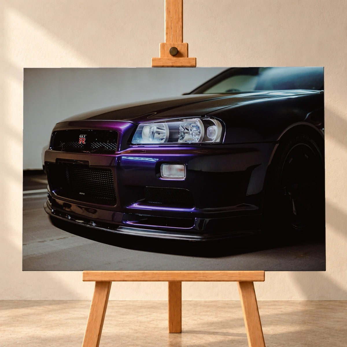 Visualisierung eines querformatigen Leinwandbilds auf einer Holzstaffelei vor heller Wand. Das Motiv zeigt die dunkelviolette Front eines Nissan Skyline GT-R R34 aus niedriger Perspektive, mit Scheinwerfer und GT-R-Emblem im Kühlergrill.