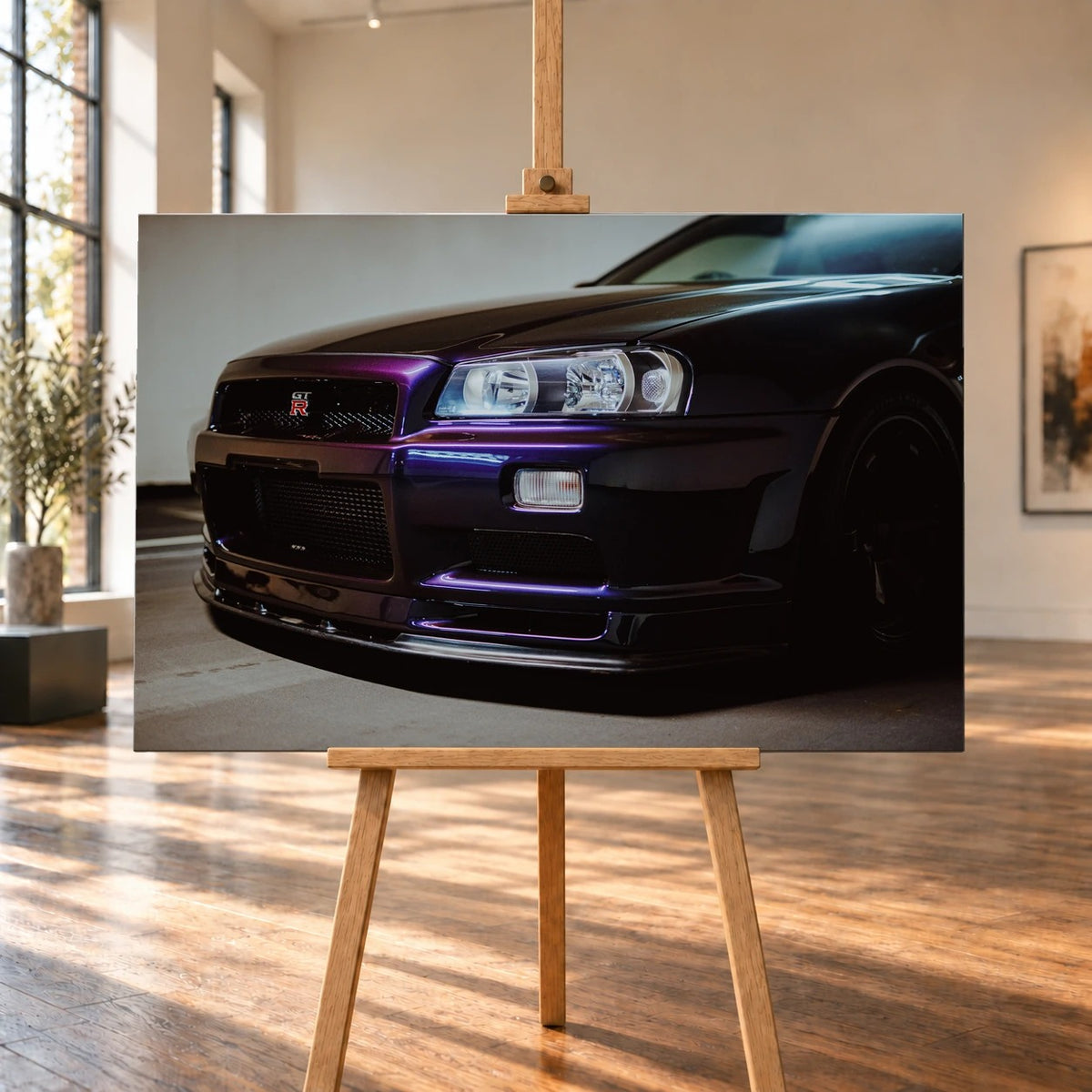 Raumvisualisierung mit einem querformatigen Leinwandbild auf einer Holzstaffelei in einem hellen Raum mit hohen Fenstern und Holzboden. Auf dem Bild ist die dunkelviolette Front eines Nissan Skyline GT-R R34 mit GT-R-Emblem zu sehen.