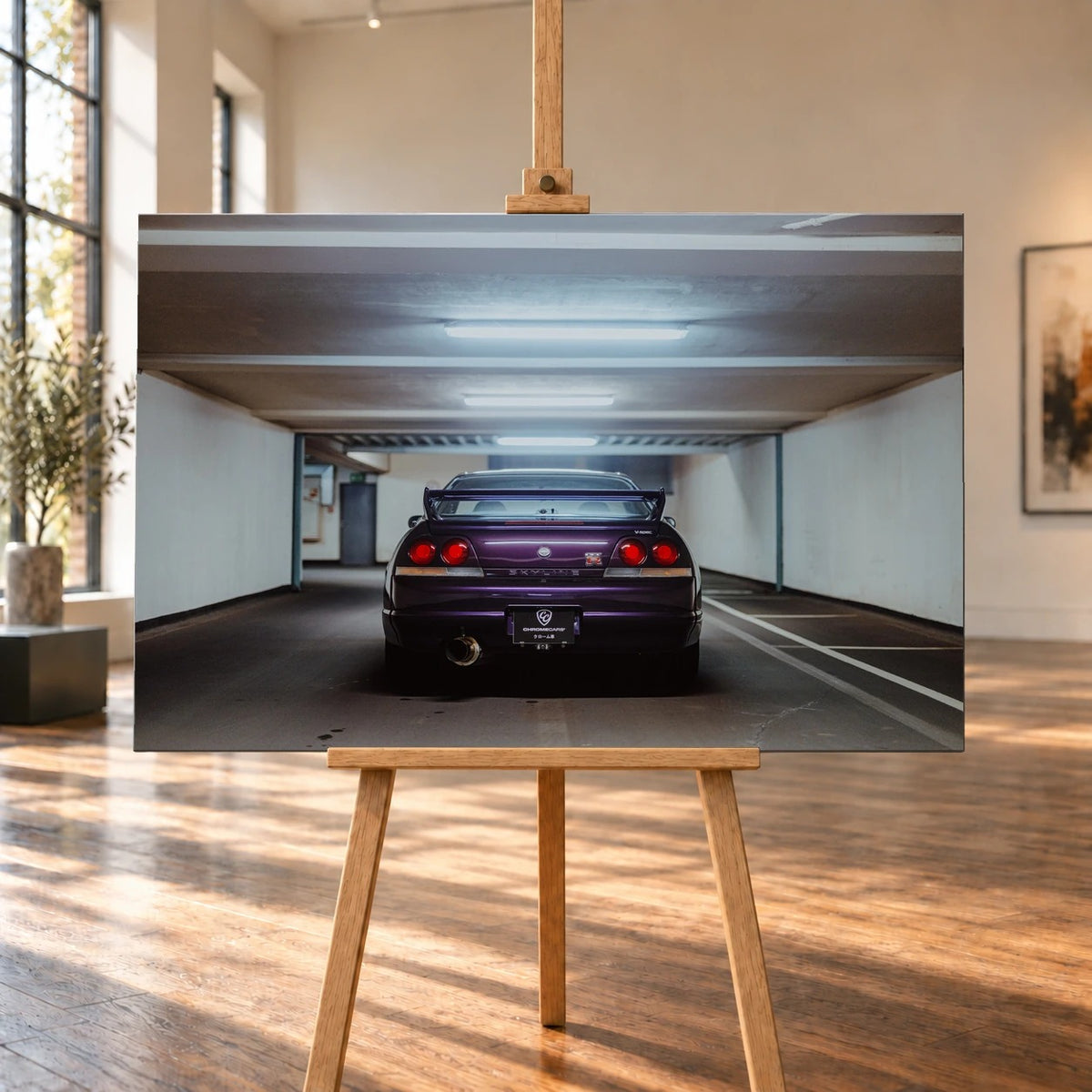 Visualisierte Raumansicht eines querformatigen Leinwandbilds auf einer Holzstaffelei in einem hellen Raum mit hohen Fenstern und Holzfußboden. Das Garagenmotiv zeigt das violette Heck eines Nissan Skyline GT-R R33 V-Spec mit vier roten Rückleuchten.