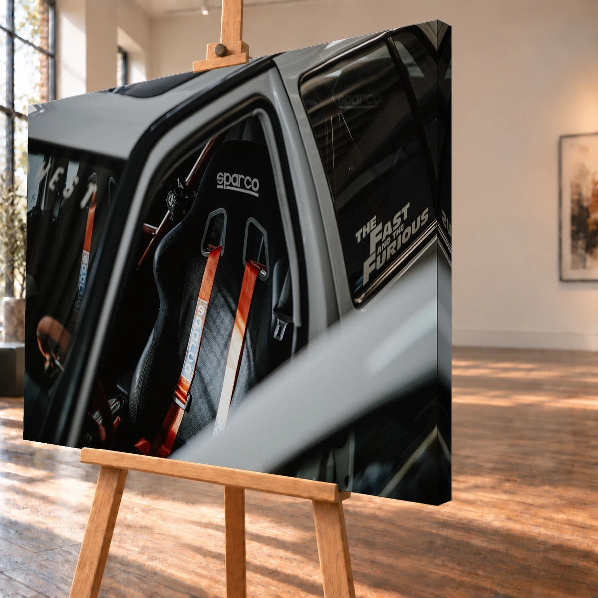 Schrägansicht eines Leinwandbilds als Visualisierung auf einer Holzstaffelei. Das Innenraummotiv von Jesses VW Jetta mit schwarzem Sparco-Schalensitz und roten Gurten setzt sich auf der sichtbaren rechten Seitenkante fort.