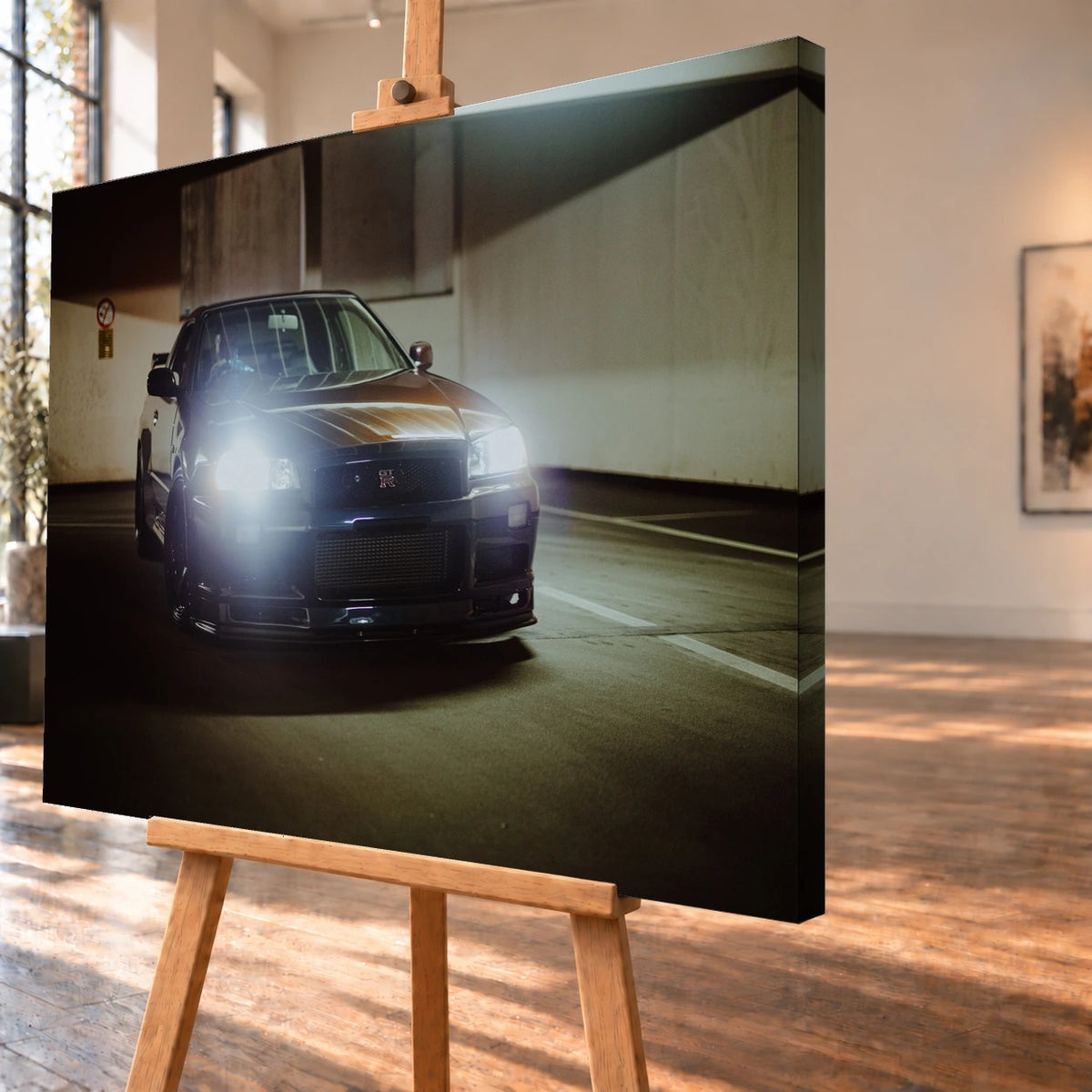 Schrägansicht eines Leinwandbilds als Produktvisualisierung auf einer Holzstaffelei. Das Motiv setzt sich auf der sichtbaren rechten Seitenkante fort und zeigt einen Nissan Skyline GT-R R34 mit eingeschalteten Scheinwerfern im Parkhaus.