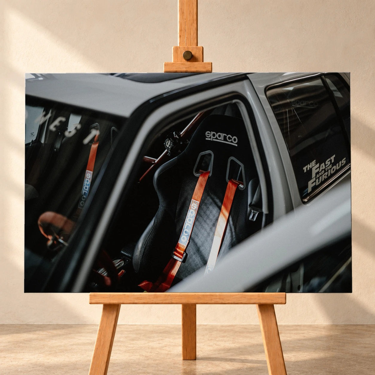 Visualisierung eines querformatigen Leinwandbildes auf einer Holzstaffelei vor heller Wand. Das Motiv zeigt den Innenraum von Jesses VW Jetta aus „The Fast and the Furious“ mit einem schwarzen Sparco-Schalensitz und roten Gurten.