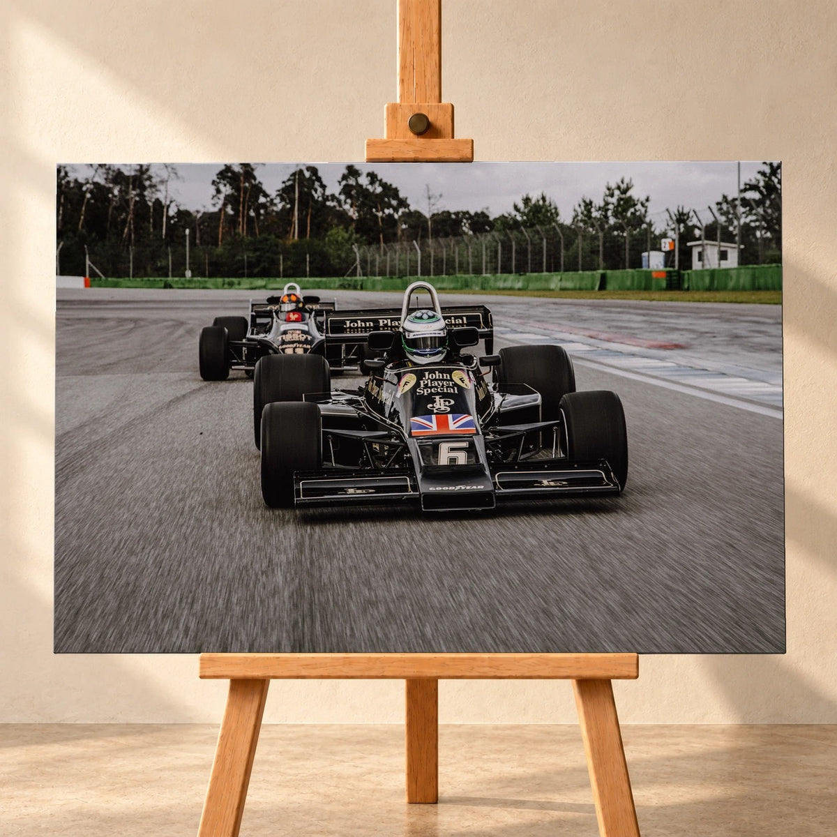 Frontale Visualisierung eines querformatigen Leinwandbildes auf einer Holzstaffelei vor heller Wand. Das Motiv zeigt Lotus 77 und Lotus 88 in Schwarz-Gold auf einer Rennstrecke, mit der Startnummer 6 am vorderen Wagen.