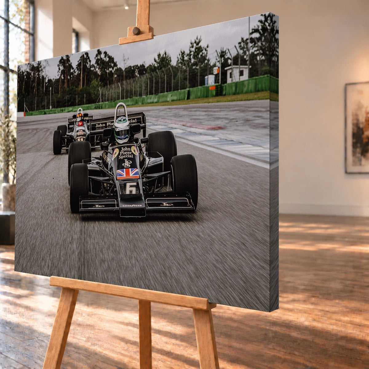Schrägansicht eines Leinwandbildes als Visualisierung auf einer Holzstaffelei, mit sichtbarer, bedruckter rechter Seitenkante. Das Rennstreckenmotiv zeigt die schwarz-goldenen Lotus 77 und Lotus 88 frontal, einen Wagen groß im Vordergrund und den zweiten links dahinter.