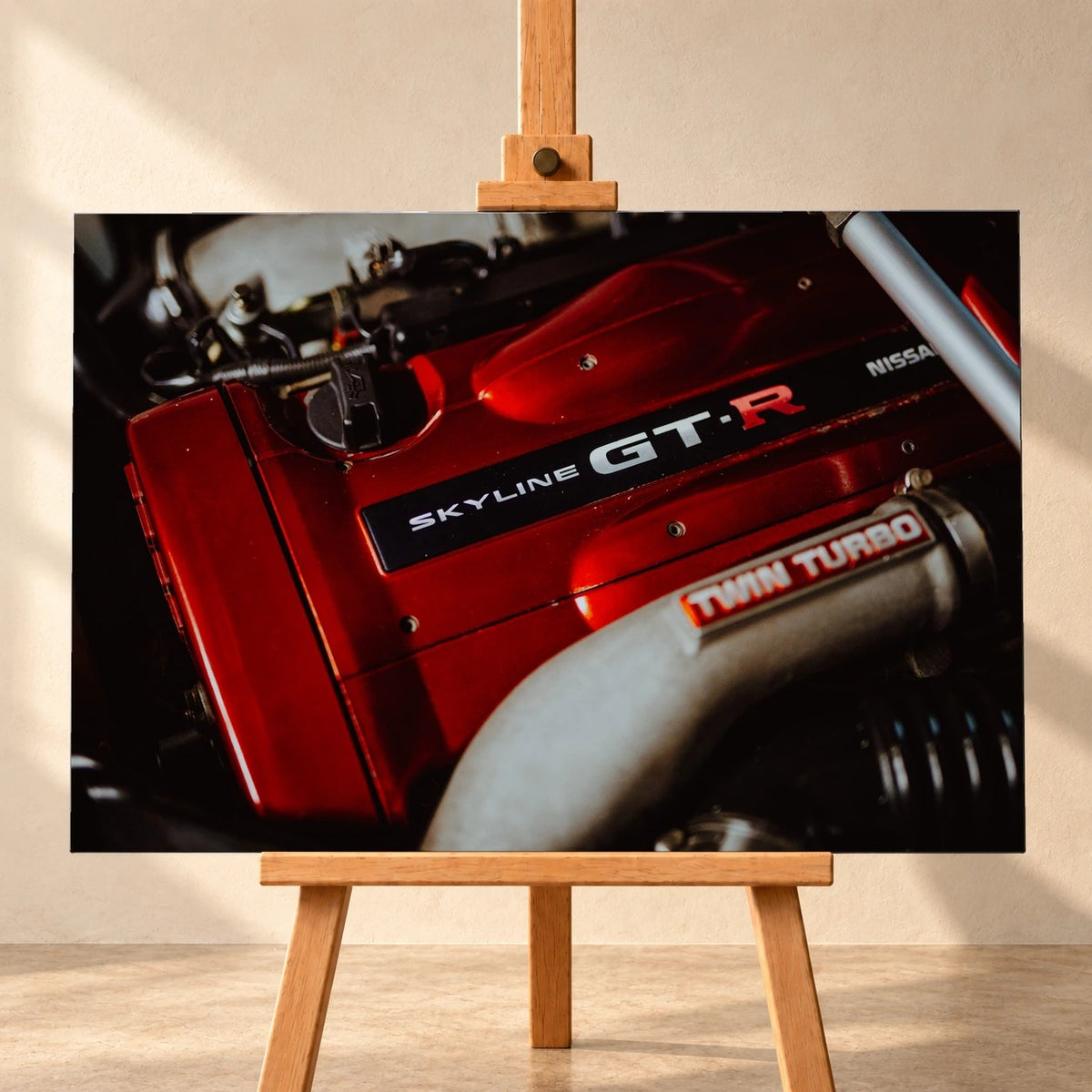 Visualisierung eines Leinwandbilds im Querformat auf einer Holzstaffelei vor heller Wand. Das Motiv zeigt die rote Motorabdeckung eines Nissan Skyline GT-R R34 mit „SKYLINE GT-R“-Schriftzug und einem silberfarbenen Rohr im Vordergrund.