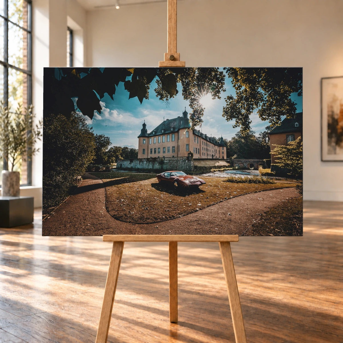 Raumvisualisierung mit einem querformatigen Leinwandbild auf einer Holzstaffelei in einem hellen Raum mit großen Fenstern und Holzboden. Auf dem Bild steht der rote Pontiac Number One vor einem von Bäumen umgebenen Schloss.
