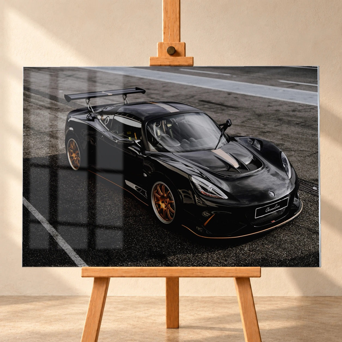Frontale Visualisierung eines Acrylglasbilds auf einer Holzstaffelei vor heller Wand. Über der linken Bildhälfte sind Fensterreflexionen dargestellt; das Motiv zeigt den schwarzen Lotus Exige 430 Cup Type 79 mit goldfarbenen Felgen schräg von vorn.