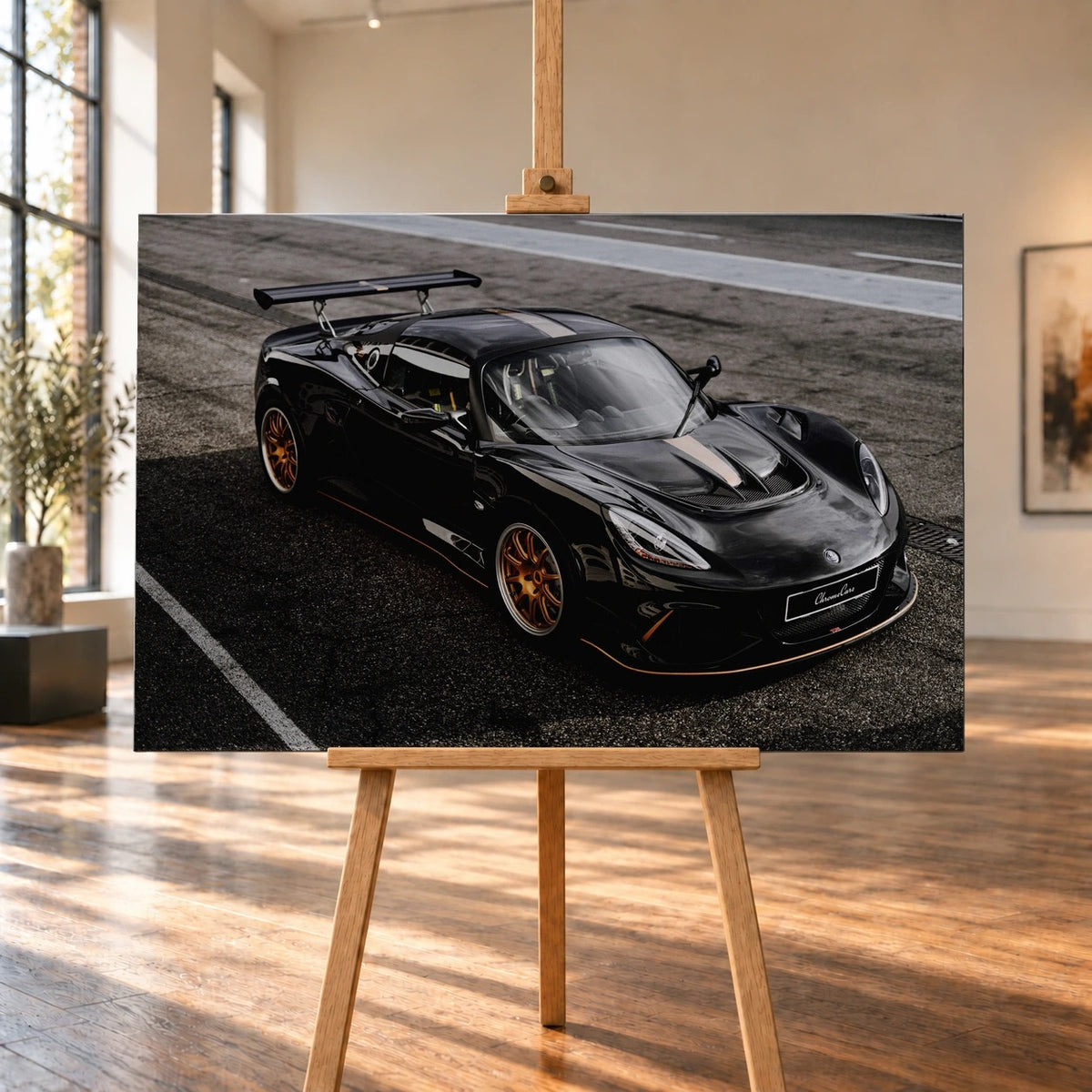 In einem hellen Raum mit hohen Fenstern und Holzboden ist ein querformatiges Leinwandbild auf einer Holzstaffelei visualisiert. Zu sehen ist der schwarze Lotus Exige 430 Cup Type 79 mit goldfarbenen Felgen und großem Heckflügel.