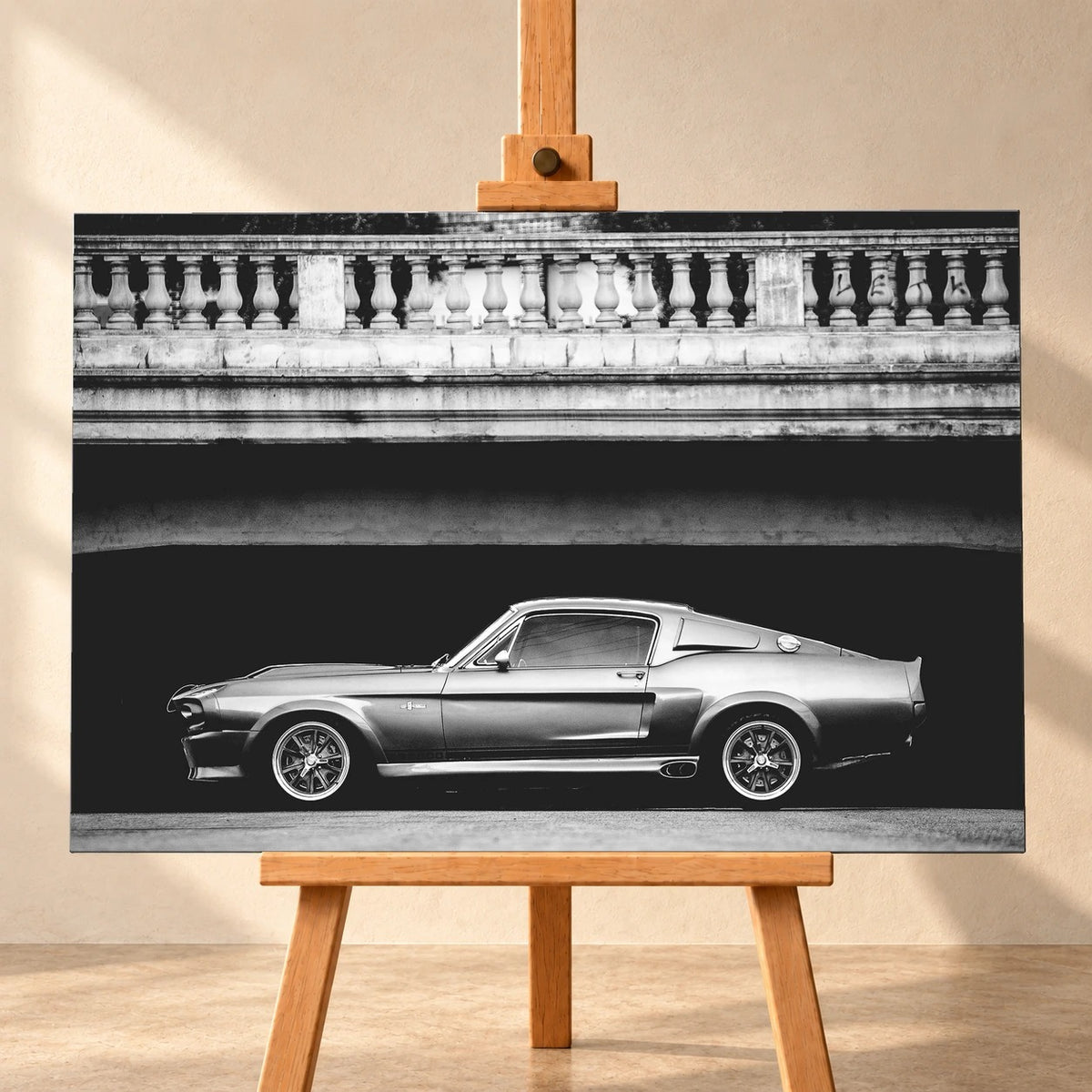 Frontal visualisiertes Leinwandbild im Querformat auf einer Holzstaffelei vor heller Wand. Das Schwarz-Weiß-Motiv zeigt Eleanor, den Ford Mustang Shelby GT500, im Seitenprofil unter einer Brücke mit steinerner Balustrade.