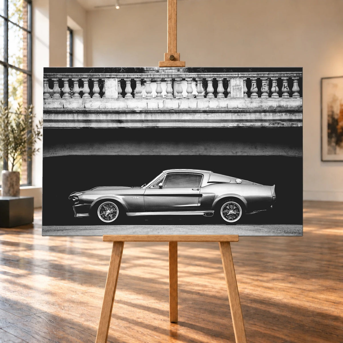 Raumvisualisierung eines querformatigen Leinwandbilds auf einer Holzstaffelei zwischen hohen Fenstern und sonnenbeschienenem Holzboden. Zu sehen ist Eleanor, der Ford Mustang Shelby GT500, in Schwarz-Weiß-Seitenansicht unter einer Brücke.