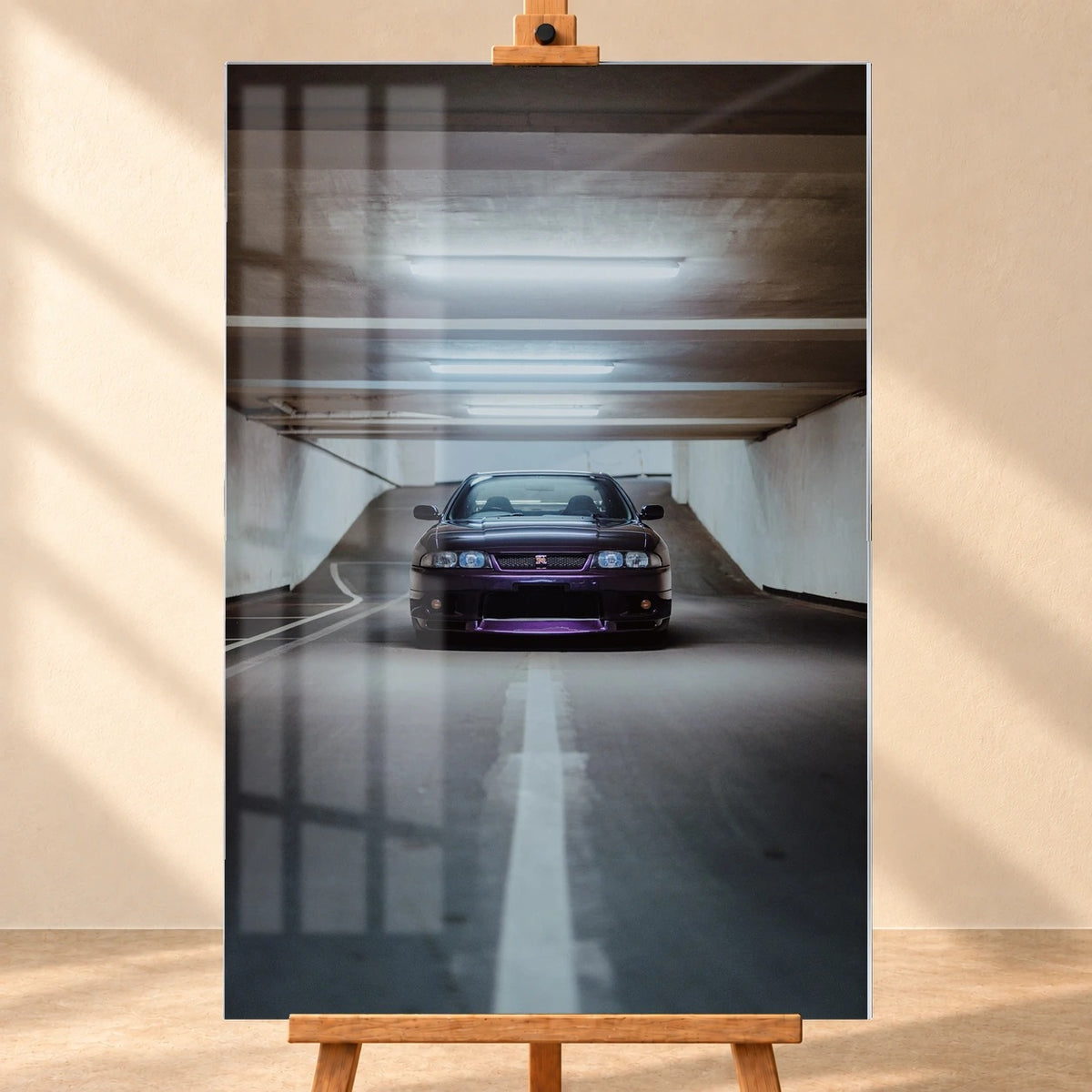 Frontalansicht eines hochformatigen Acrylglasbilds als Visualisierung auf einer Holzstaffelei. Fensterreflexionen liegen über dem Motiv eines dunkelvioletten Nissan Skyline GT-R R33 in einer beleuchteten Tiefgarage.